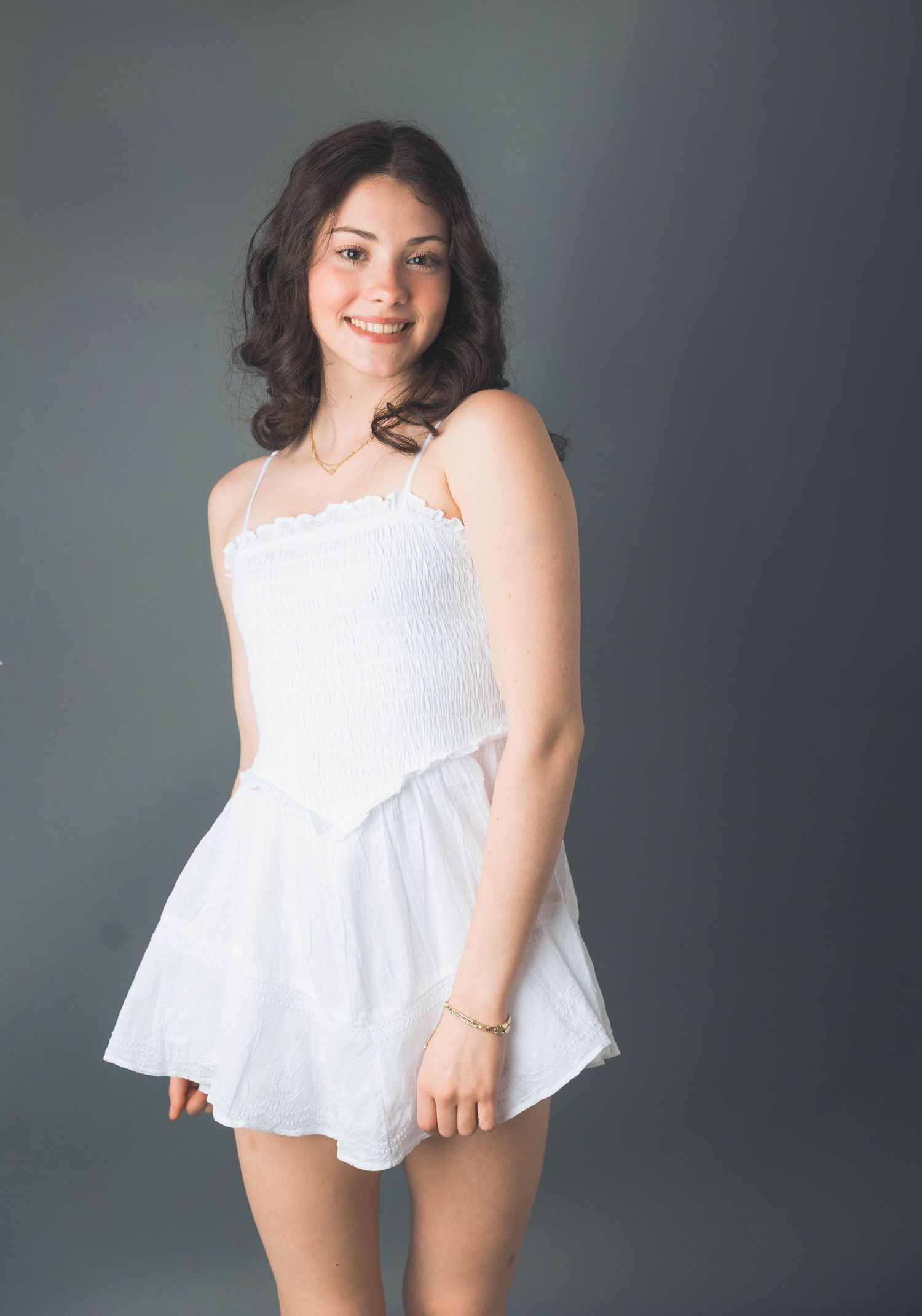 Studio portrait series featuring white eyelet dress against dark grey background.