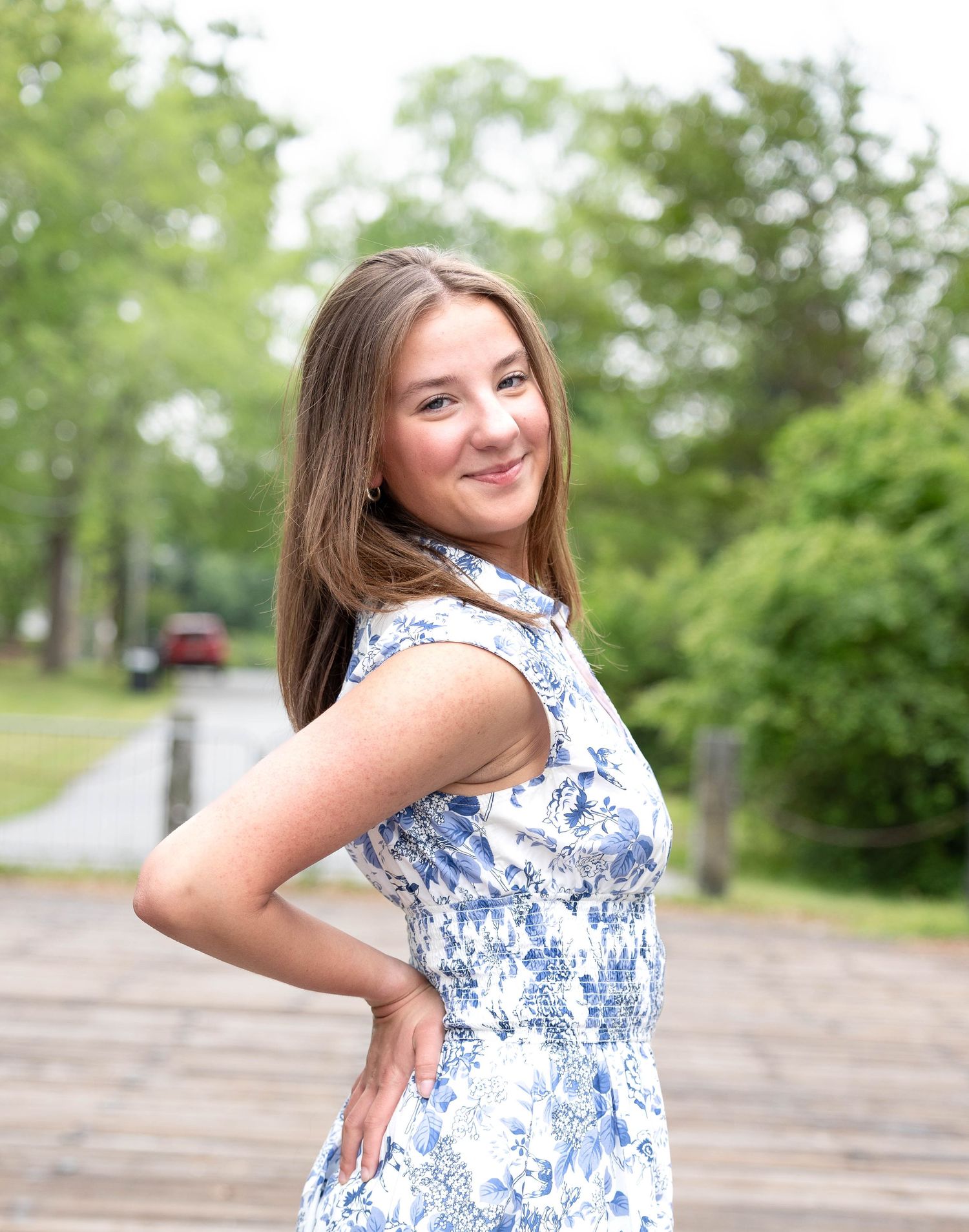 Woman in blue and white floral summer dress poses in outdoor setting with trees.