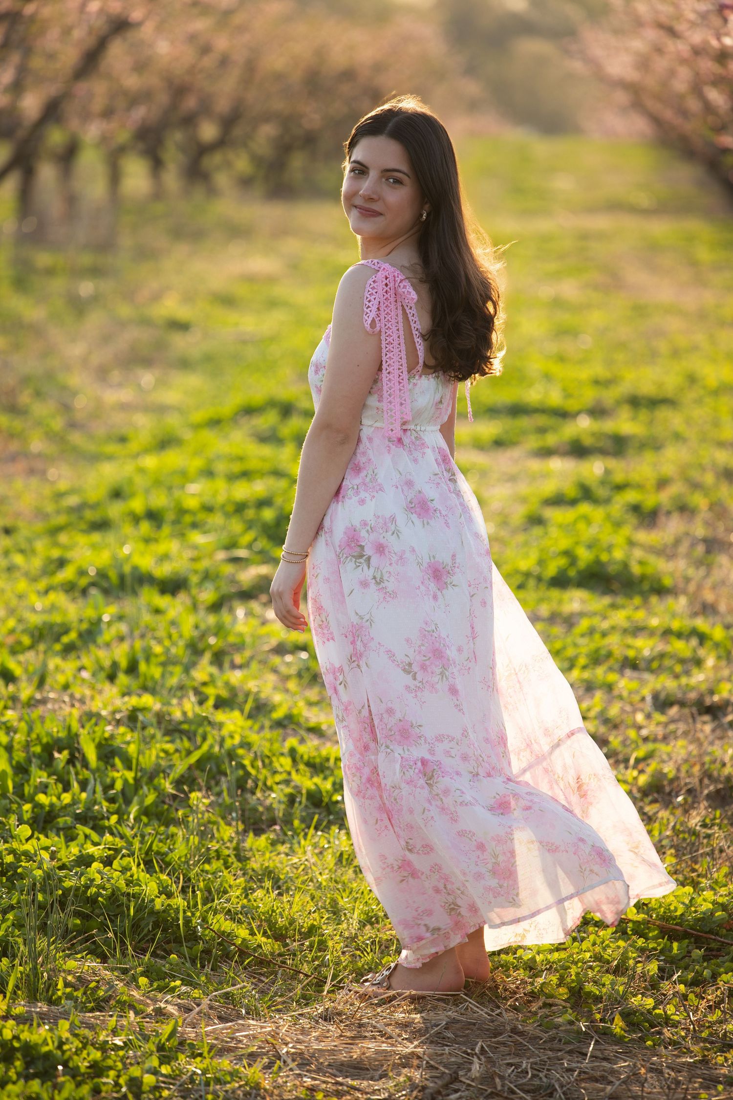 A pink floral dress flows in the sunlight as someone walks through a grassy meadow during golden hour.