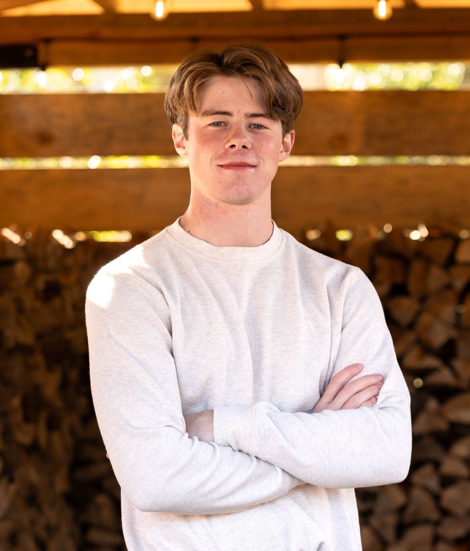 Person in white sweater posing against blurred background with warm lighting and rustic wood elements.