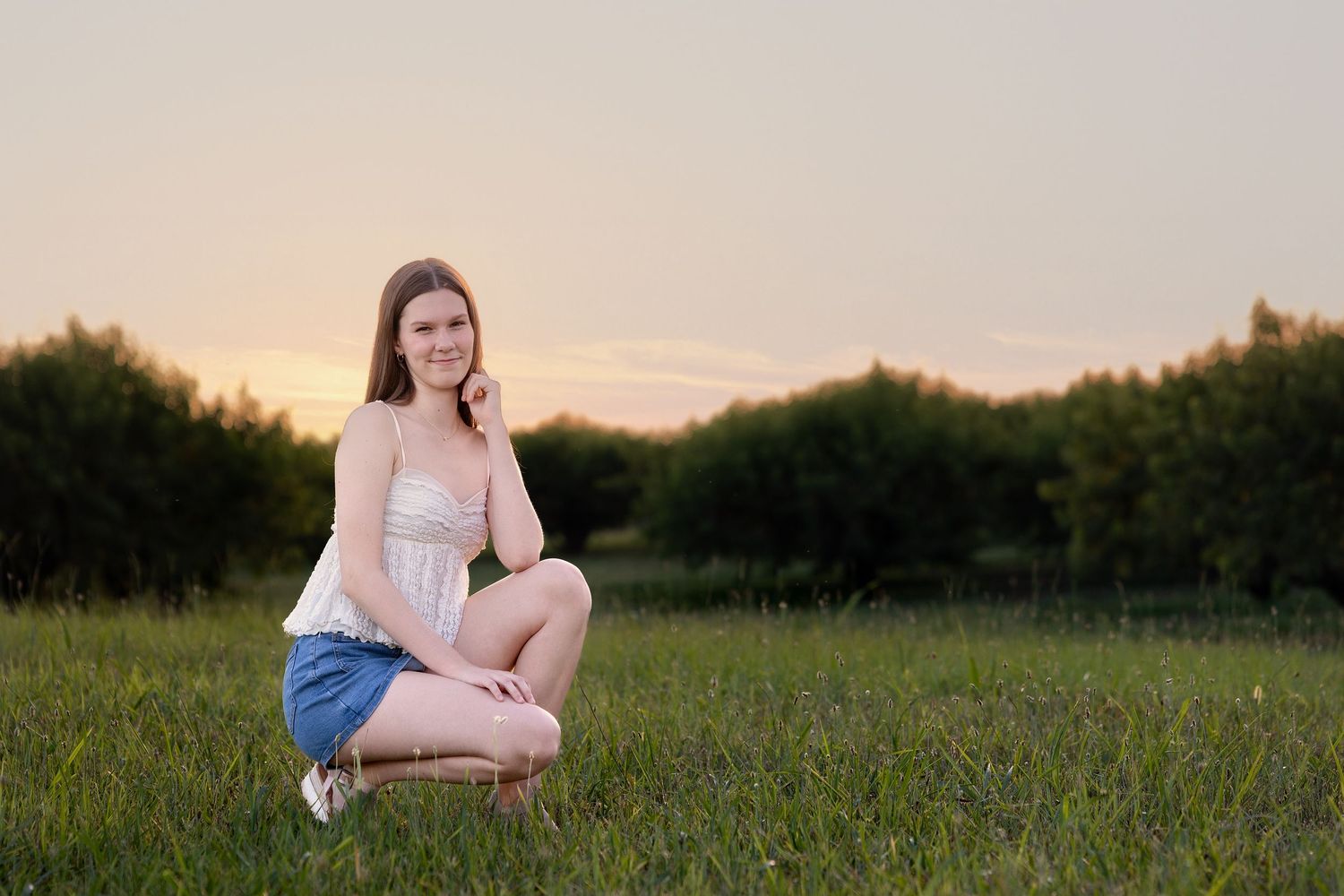 Person sitting in a grassy field at sunset wearing denim shorts and white top.