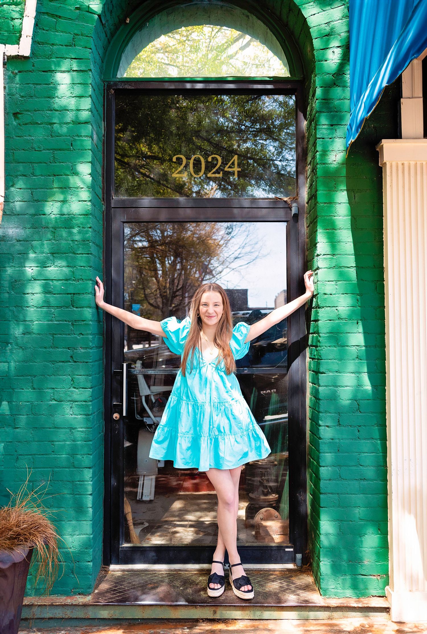 Playful poses in front of green painted building with blue dress and dramatic gestures.