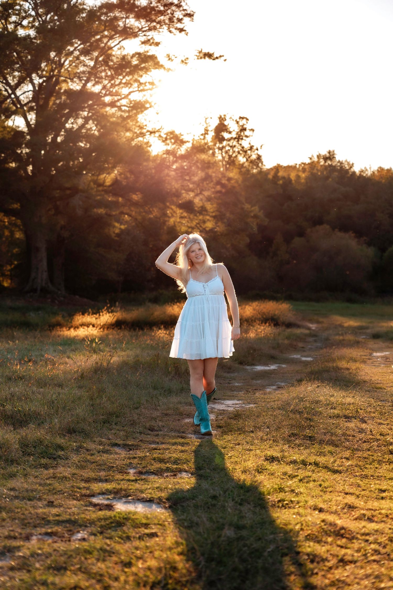 Silhouette of someone in a white dress walking through a golden sunset field with long shadows cast on the grass.