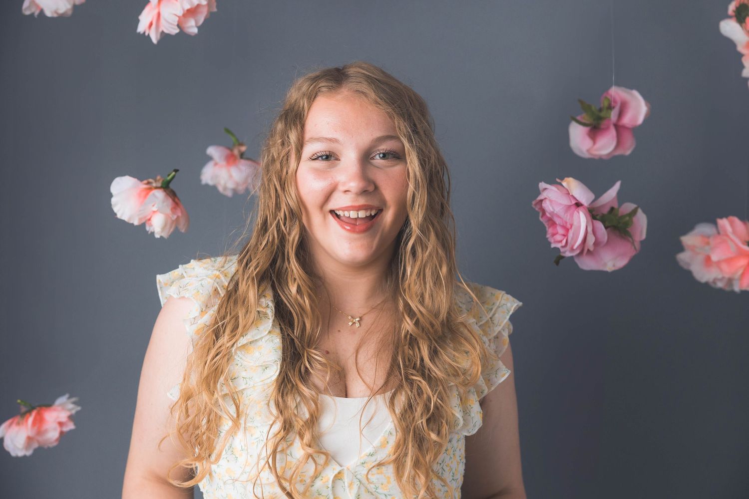 Studio portrait with floating pink flower petals against grey background.