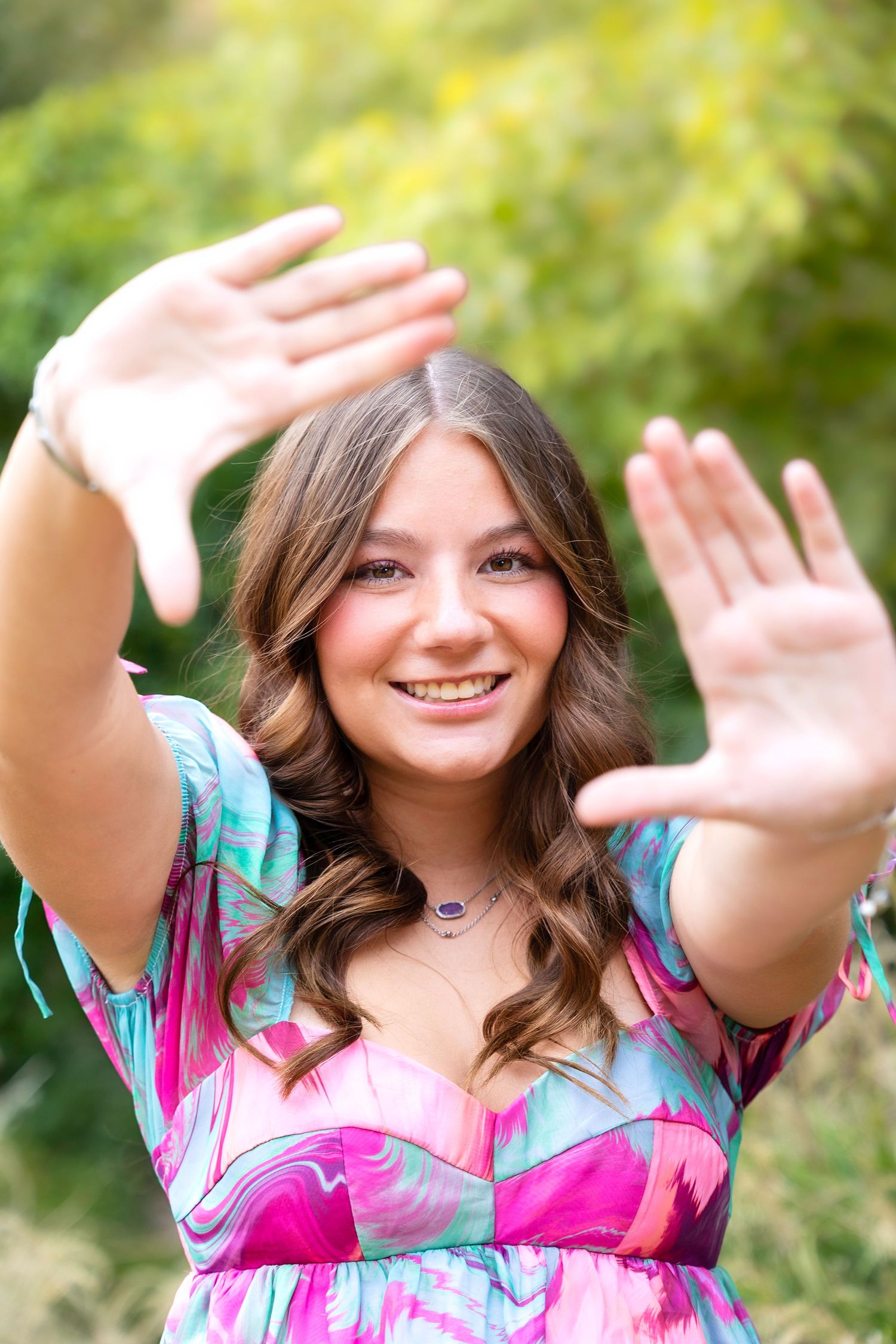 Playful portrait with hands raised in a colorful floral dress against a blurred green background.