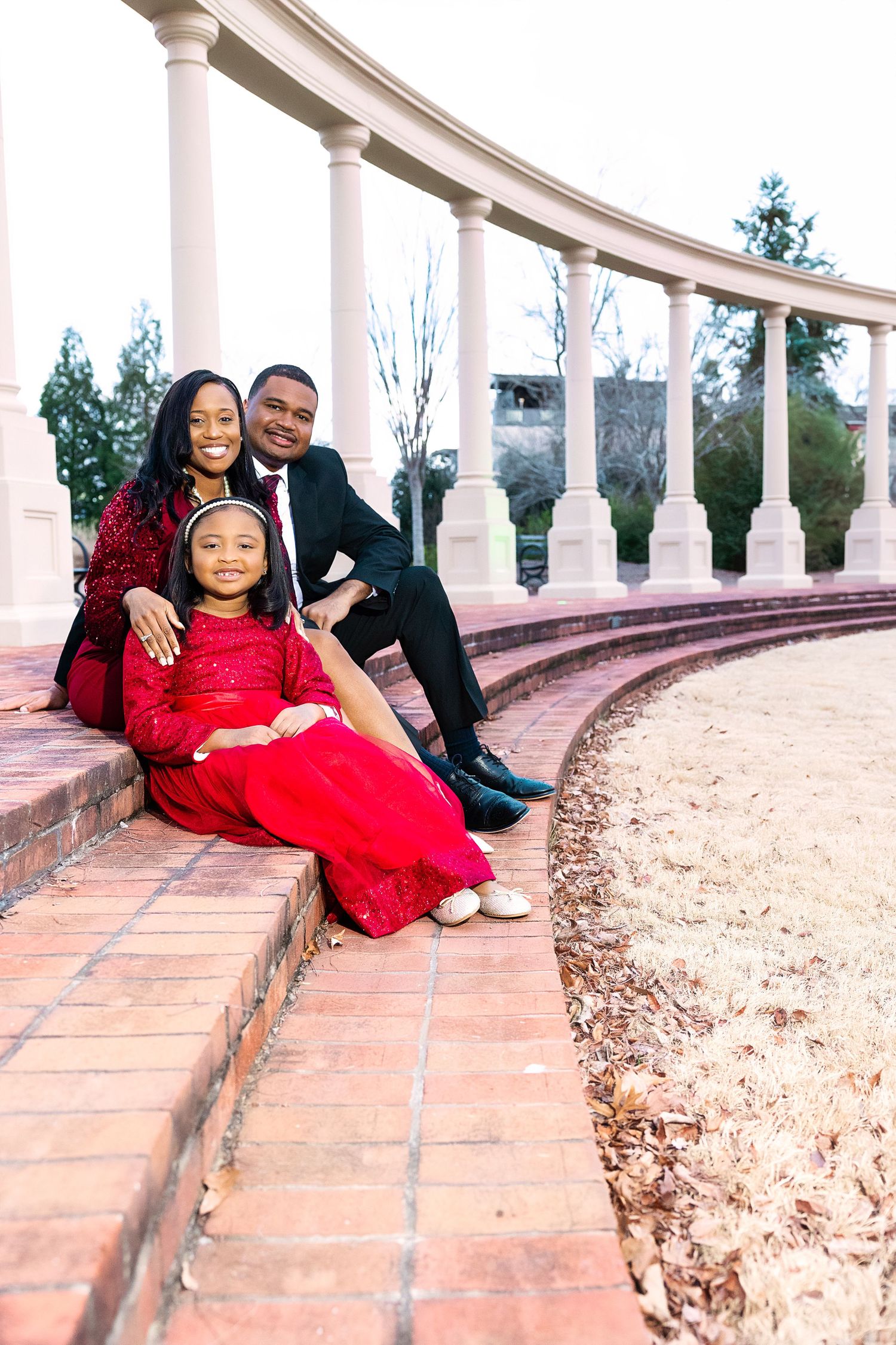 Portrait session at curved colonnade with red dress against architectural backdrop.