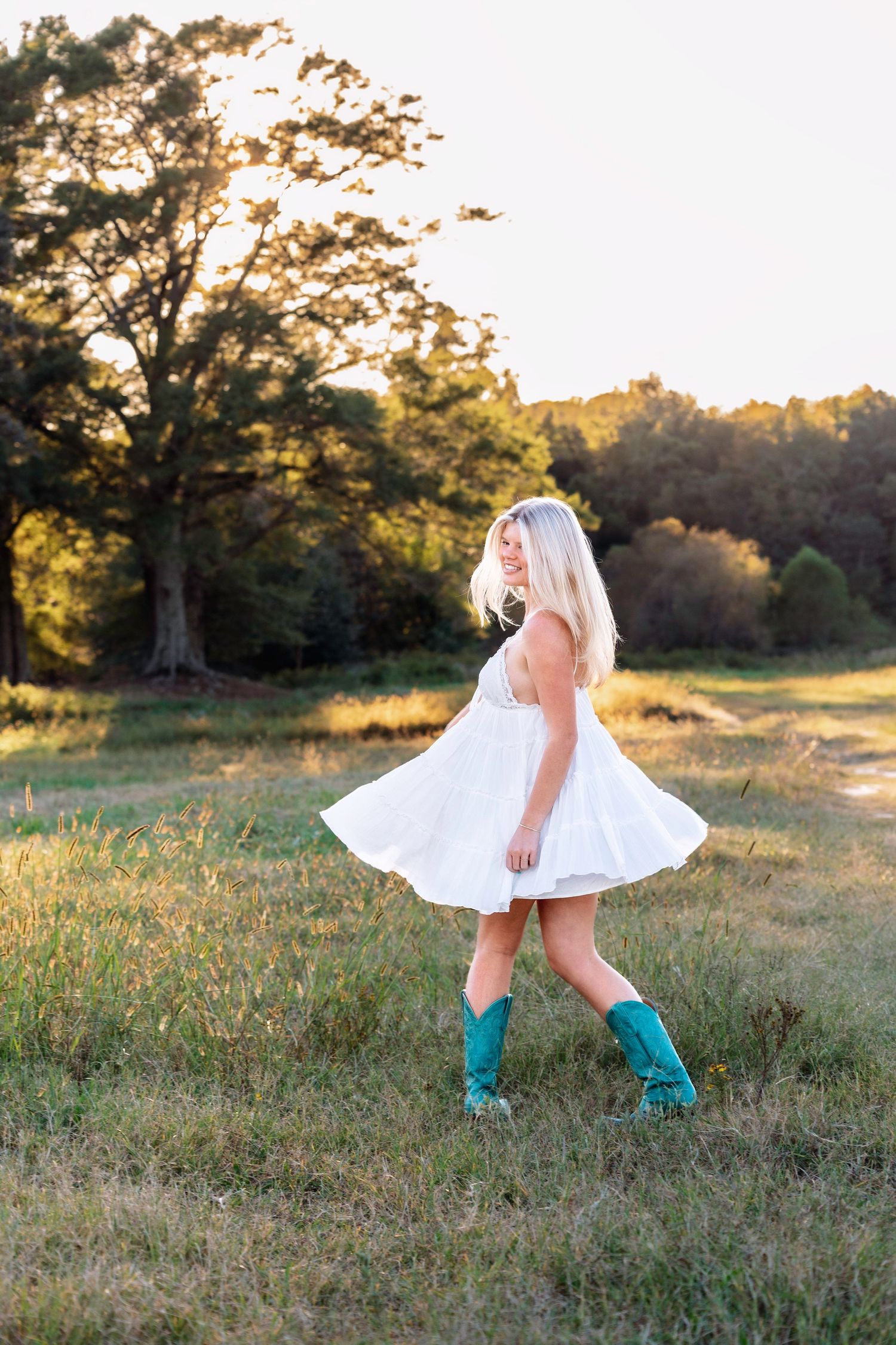 A figure in a white dress twirls in a sunlit field while wearing turquoise boots at golden hour.