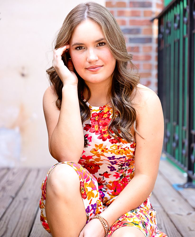 Portrait series in floral red dress against brick wall and green railing background.