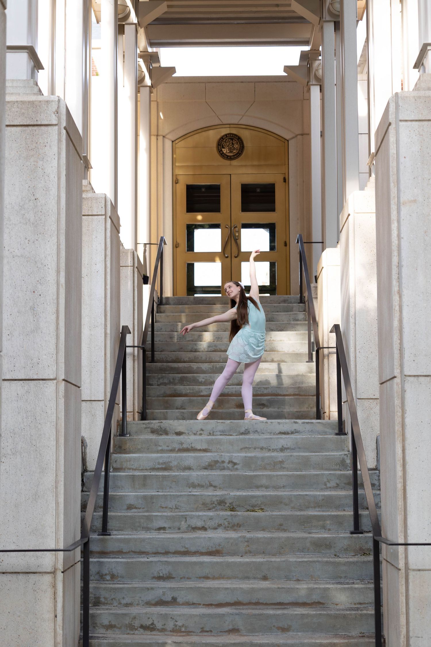 A ballet dancer performs graceful poses on stone steps leading to a columned entrance of a historic building.
