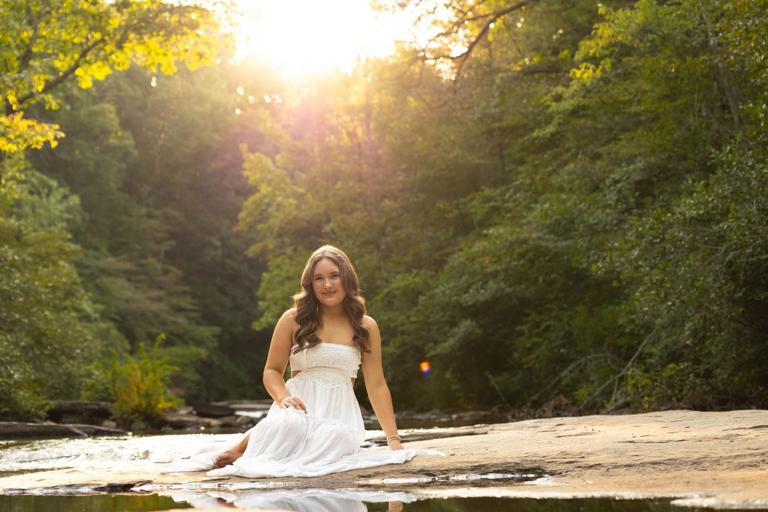 Golden sunlight streams through trees at a scenic river rock location during a summer evening photoshoot.