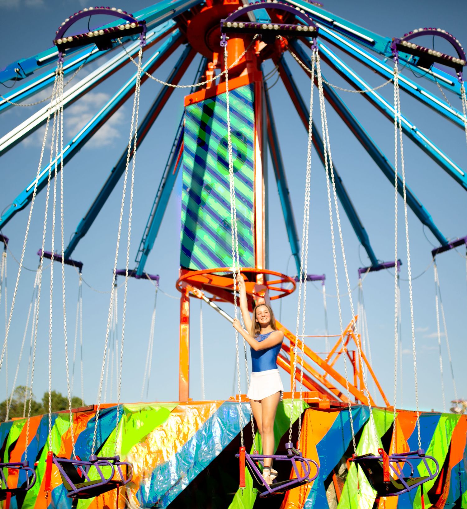 Colorful fairground swing ride with vibrant blue and orange decorations against bright blue sky.
