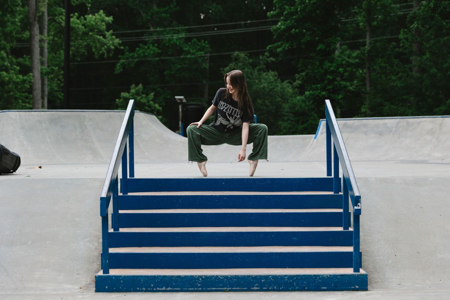 A skateboarder performs a backside boardslide down a blue handrail at a skate park.