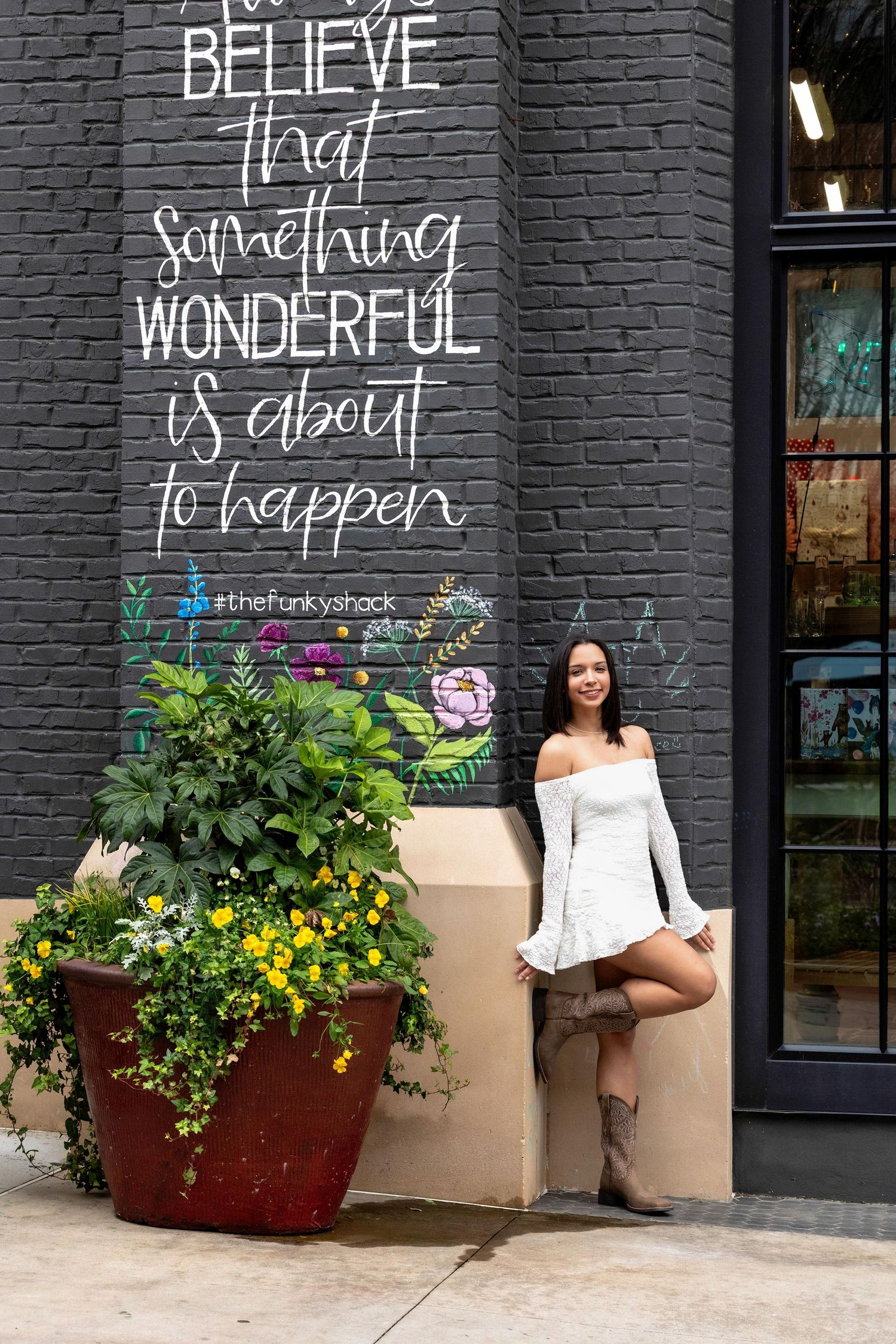 Inspirational wall text reading 'Believe something wonderful is about to happen' with decorative planter on brick wall.
