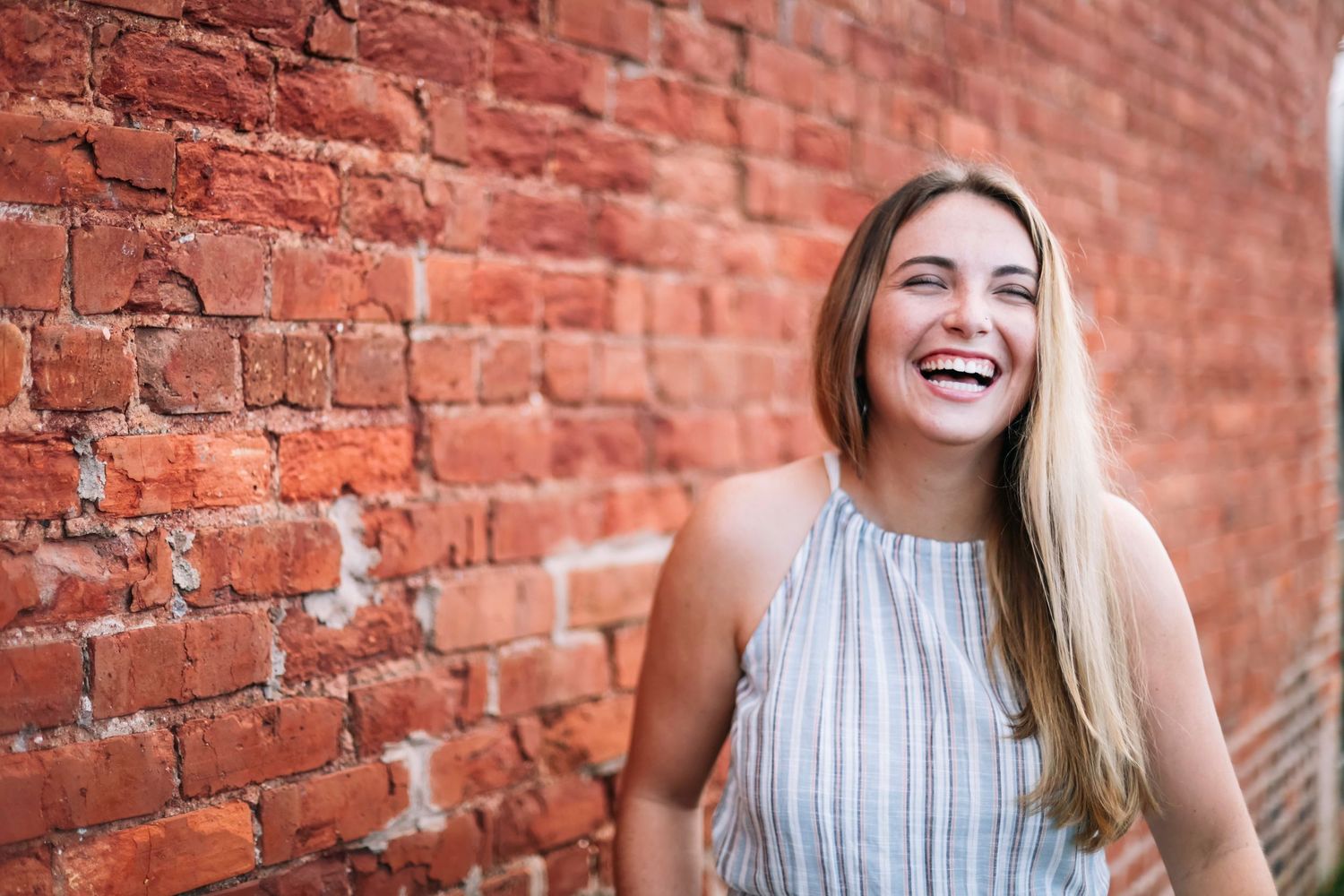 Woman laughing against a rustic red brick wall background.