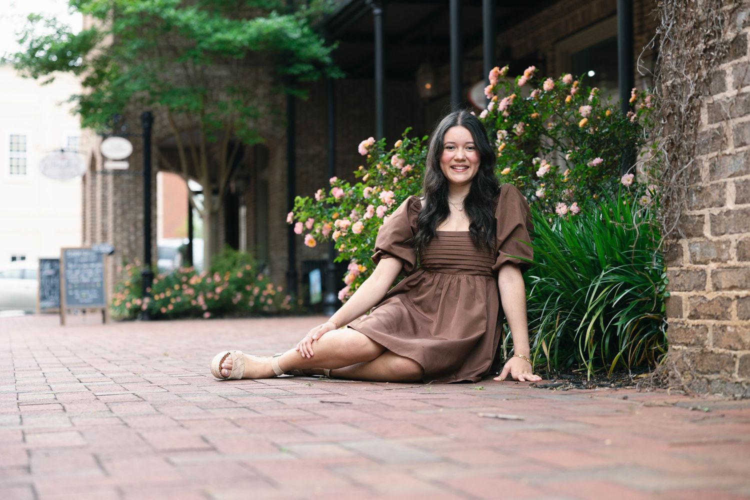 A person sits casually on stone steps surrounded by greenery and brick walls in an outdoor setting.