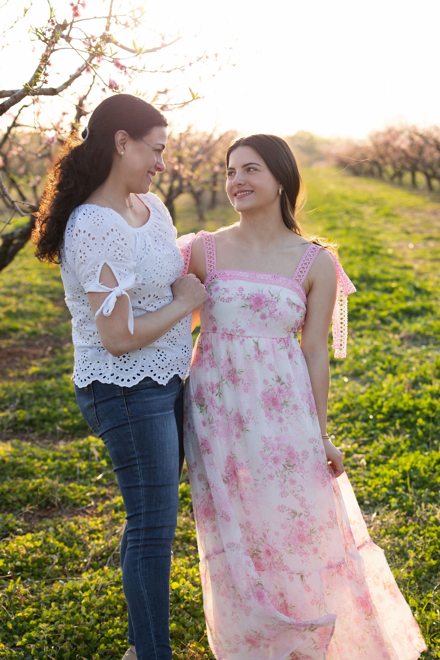 Two people share a tender moment in a spring meadow wearing white and floral dresses at sunset.