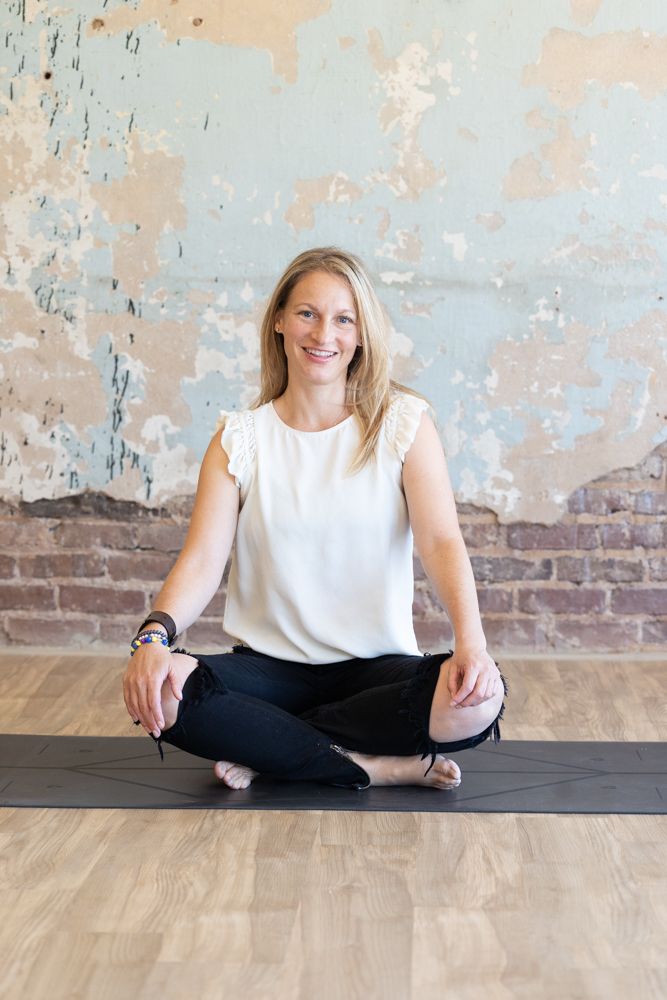 Yoga poses on wooden floor against distressed wall in white sleeveless top.