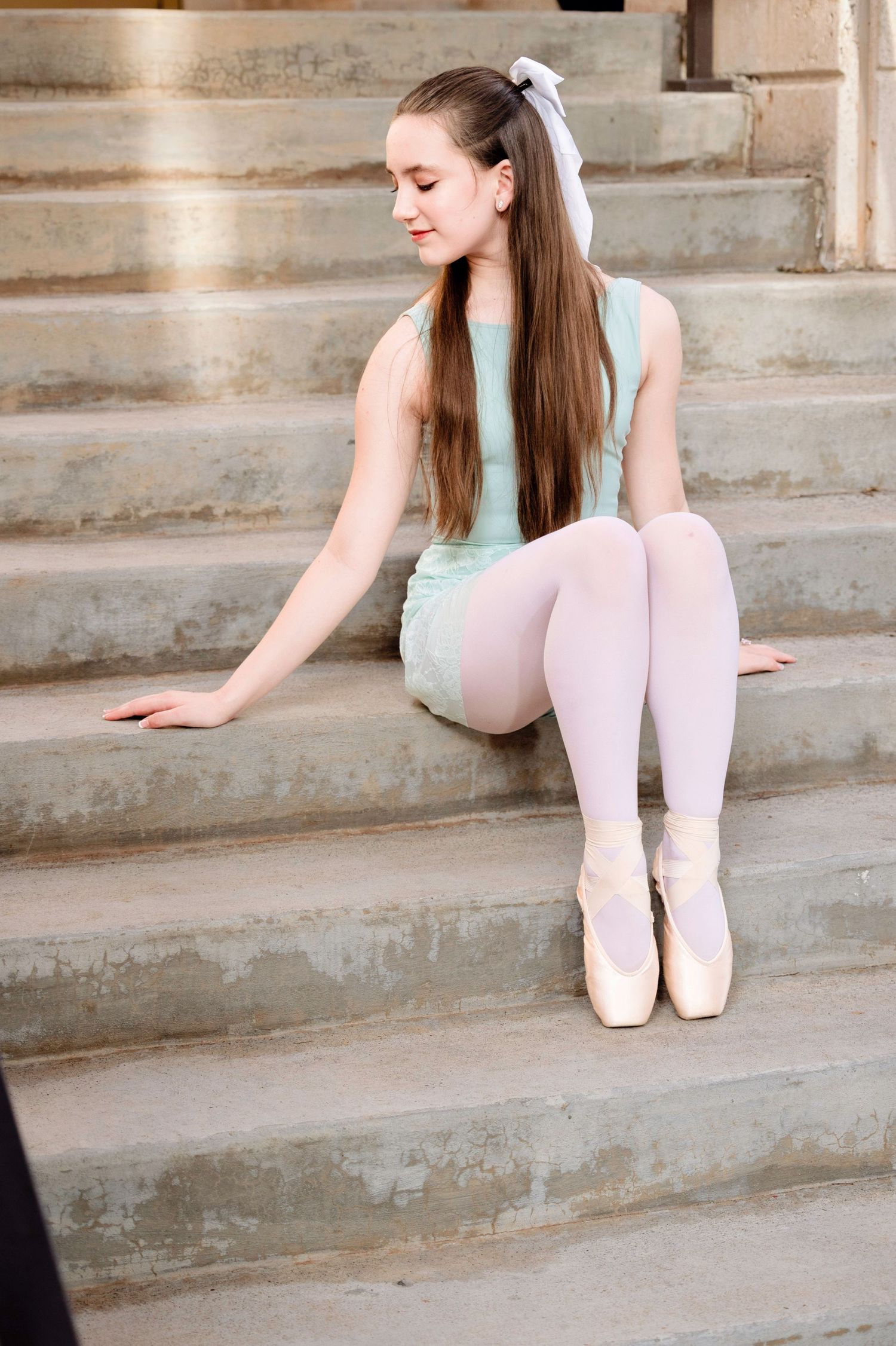 Ballet dancer in mint leotard and pink tights sits gracefully on concrete steps in a series of elegant poses.