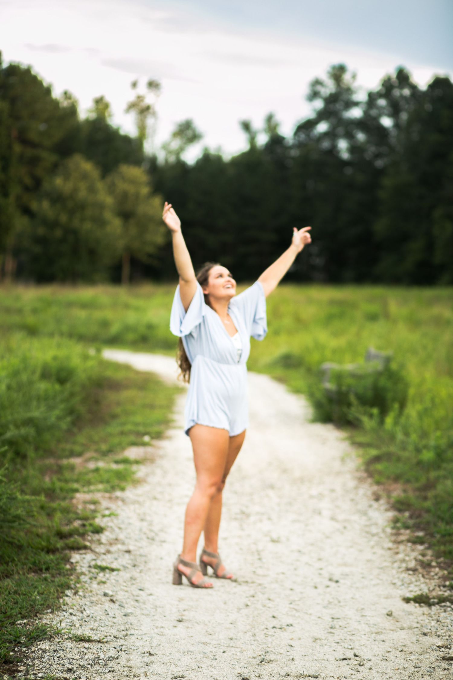 Person in white outfit celebrates joyfully on a gravel path surrounded by green fields.
