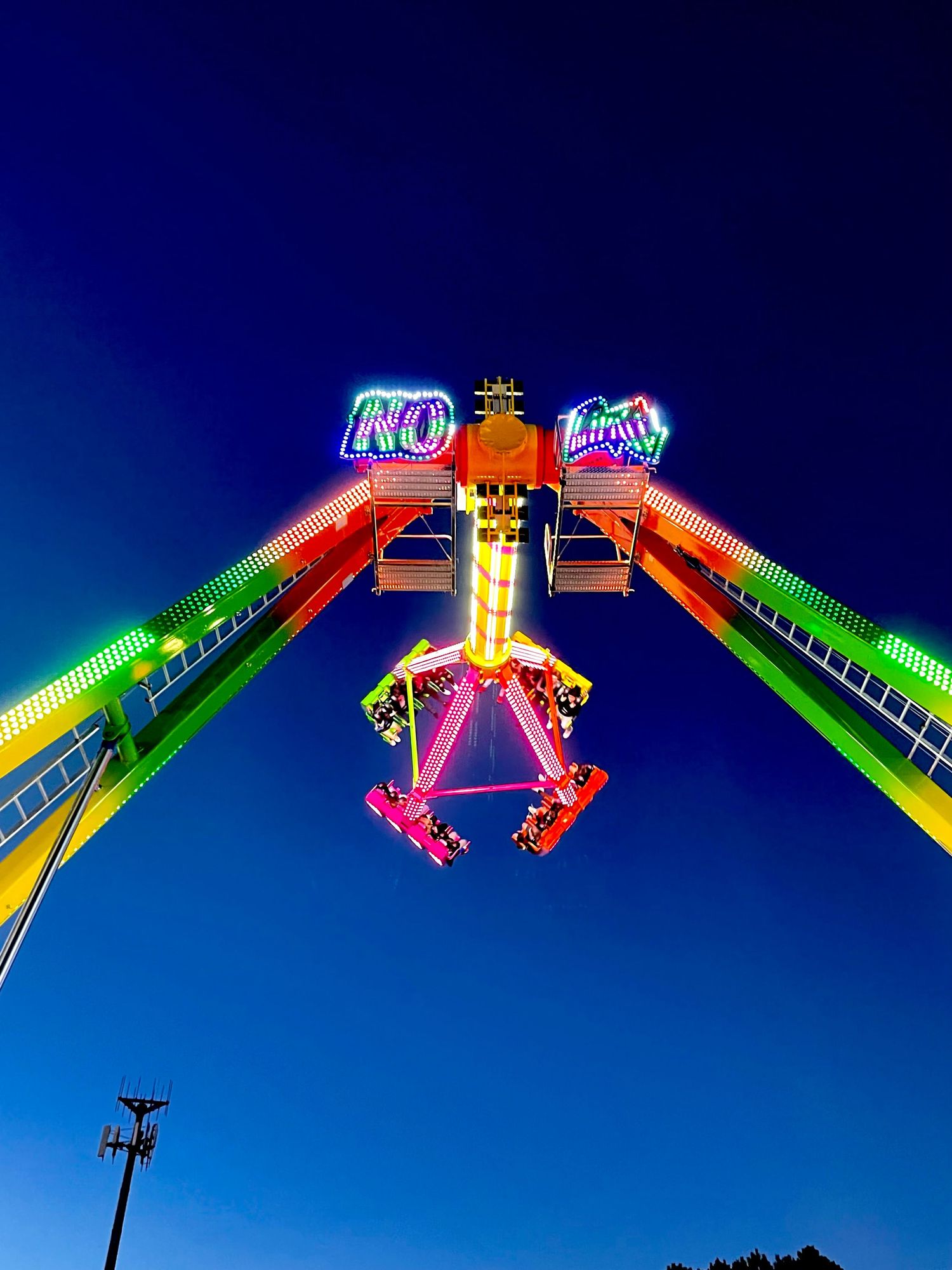 Neon carnival ride silhouetted against deep blue twilight sky.