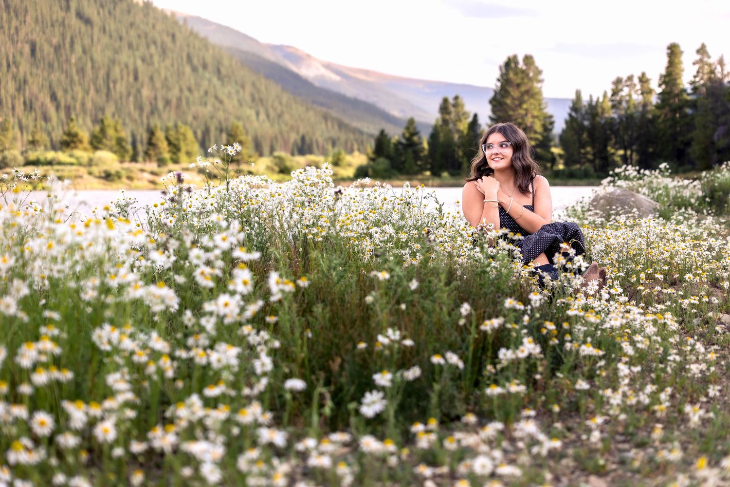 Person in dark dress amid field of white daisies with mountains in background.