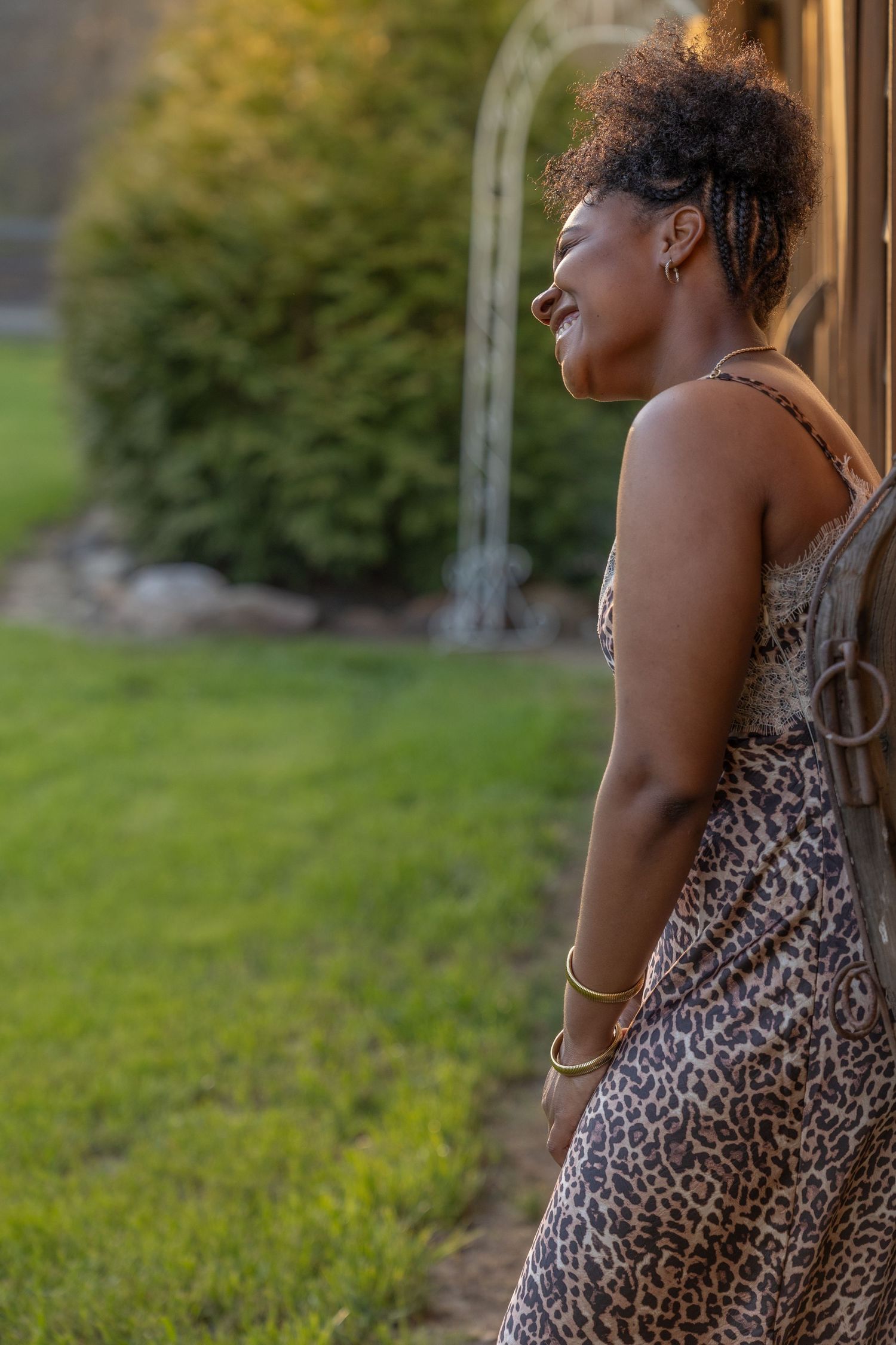 Woman in leopard print dress leaning against wooden wall outdoors in golden hour light.