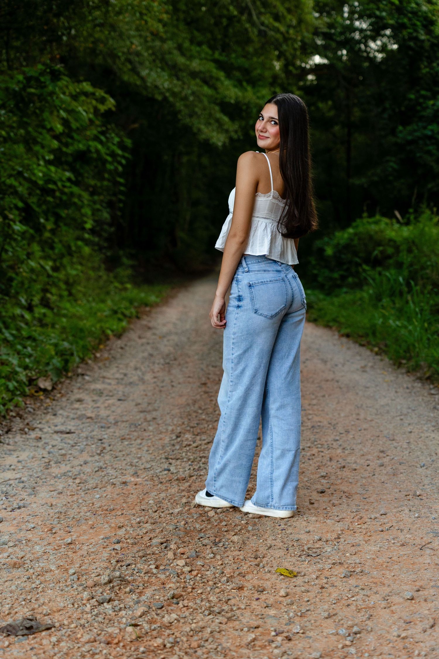 A casual outdoor portrait session on a gravel path surrounded by lush green foliage.