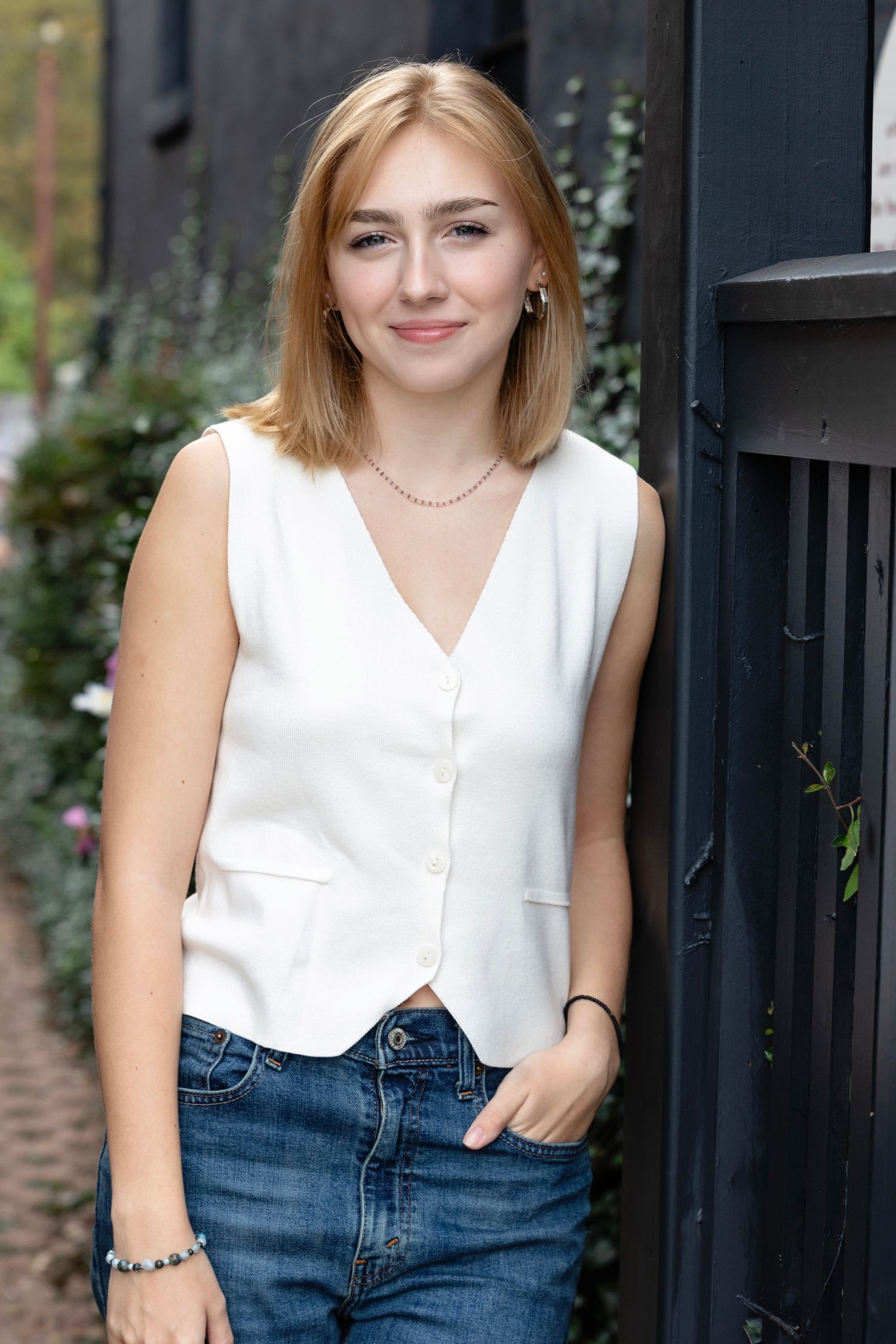 Casual portrait in white sleeveless top and jeans against black gate backdrop.