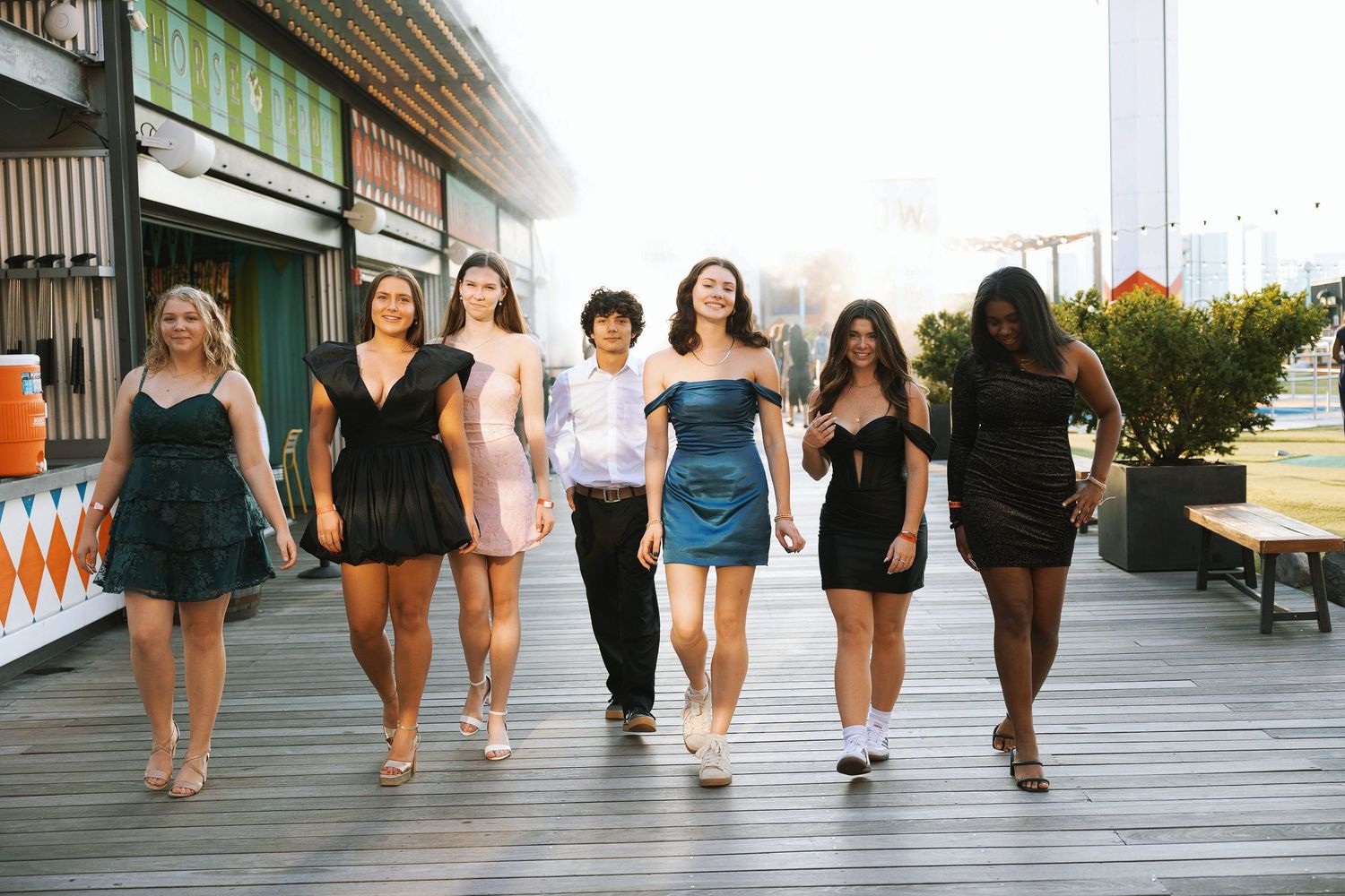A row of people walking in black and white outfits shown from the waist down on a wooden boardwalk.