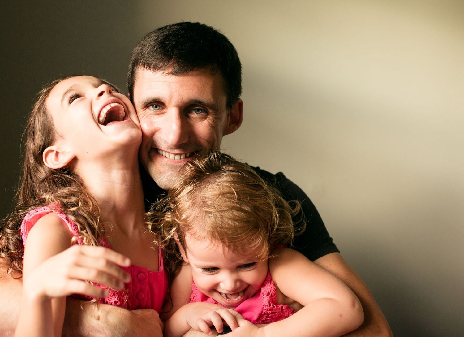 A playful family moment with laughter and affection against a neutral background.