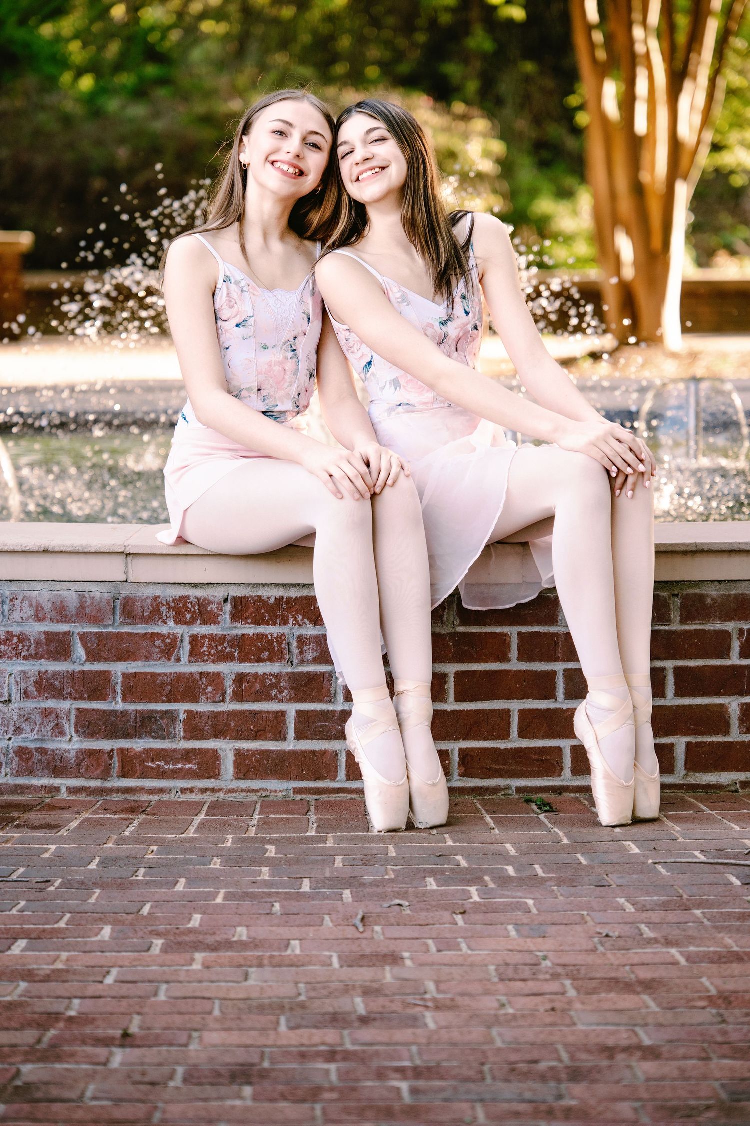 Two people in light colored outfits sit together on brick steps in a sunlit outdoor setting.