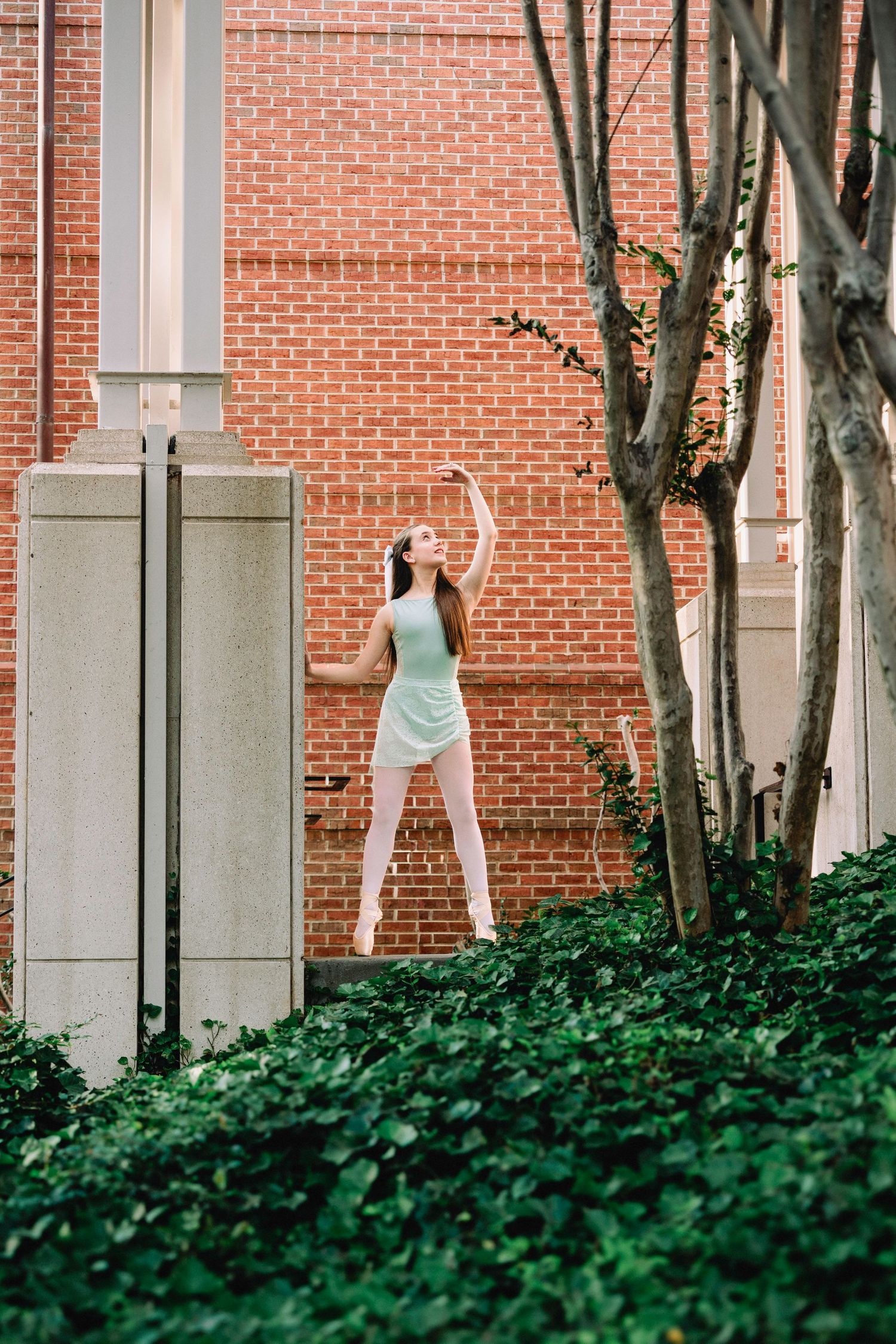 Person in dance poses against brick wall with trees in an artistic sequence.