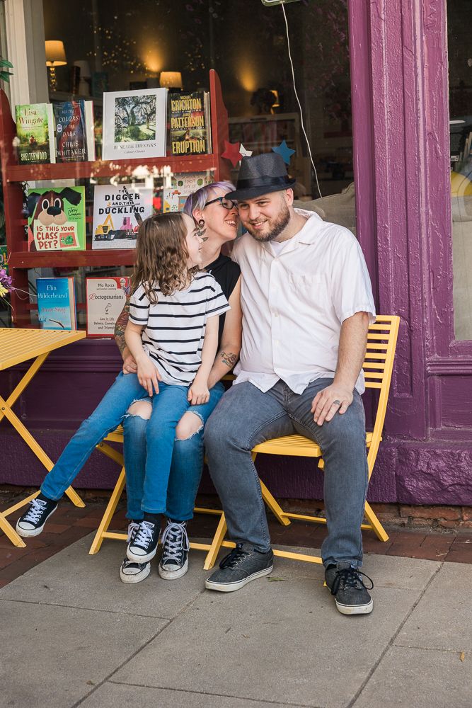 Family relaxing on yellow wooden chairs outside storefront with purple trim.