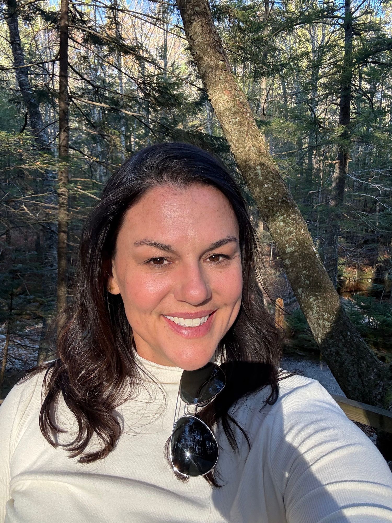 A series of selfies taken in a wooded forest setting shows someone in a white sweater smiling at the camera.