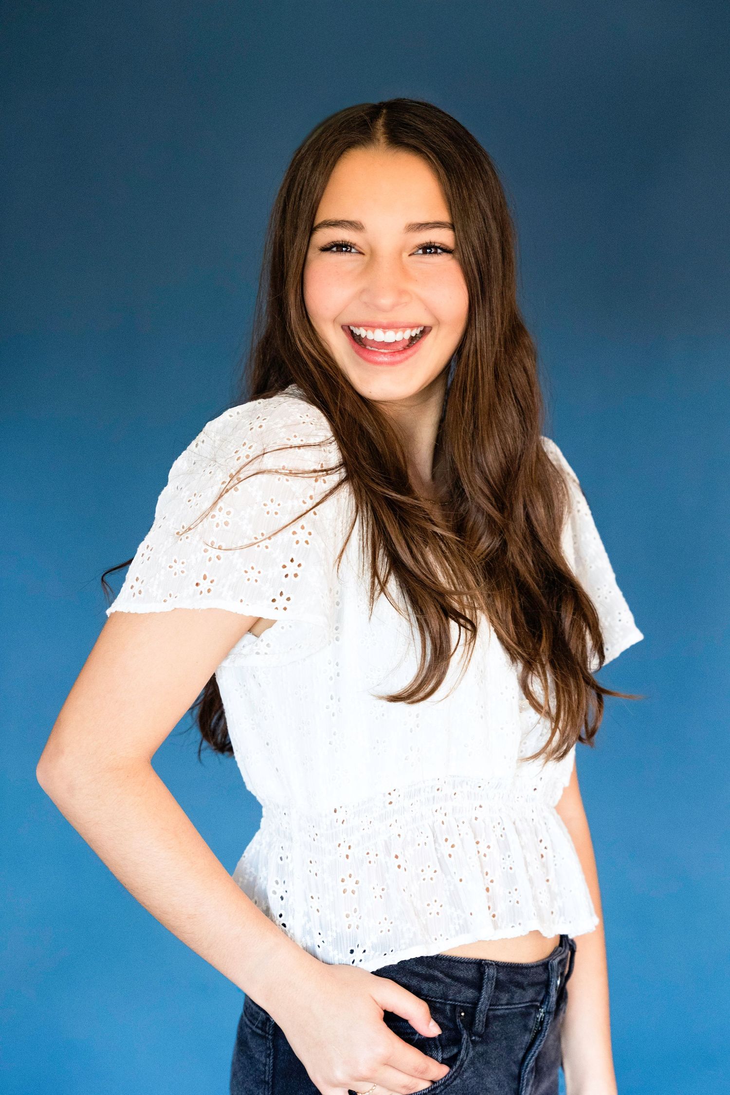 Fashion portraits against blue backdrop featuring white eyelet top and denim outfit.