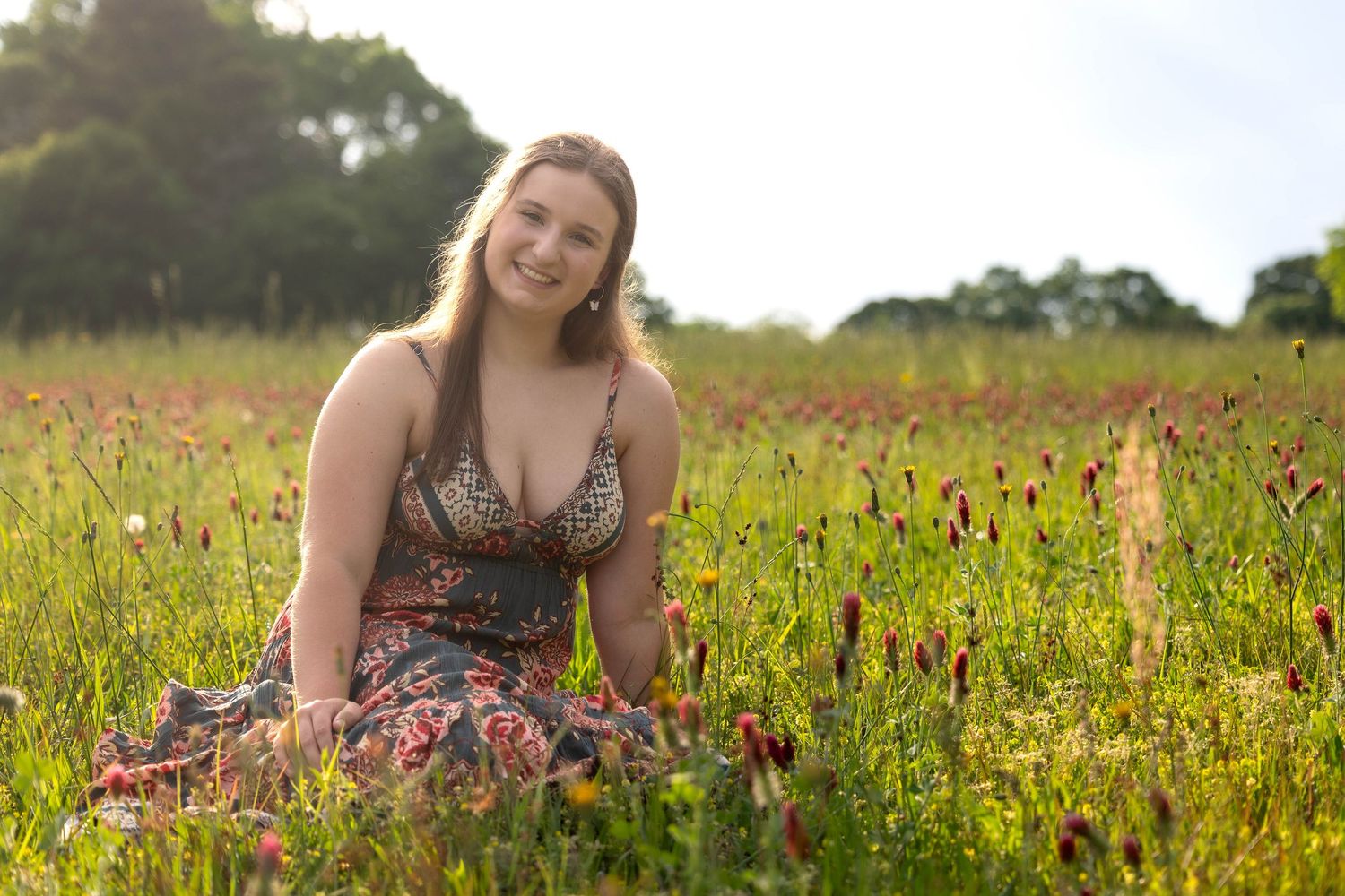 A person in a floral dress lies in a vibrant meadow filled with red wildflowers on a sunny summer day.