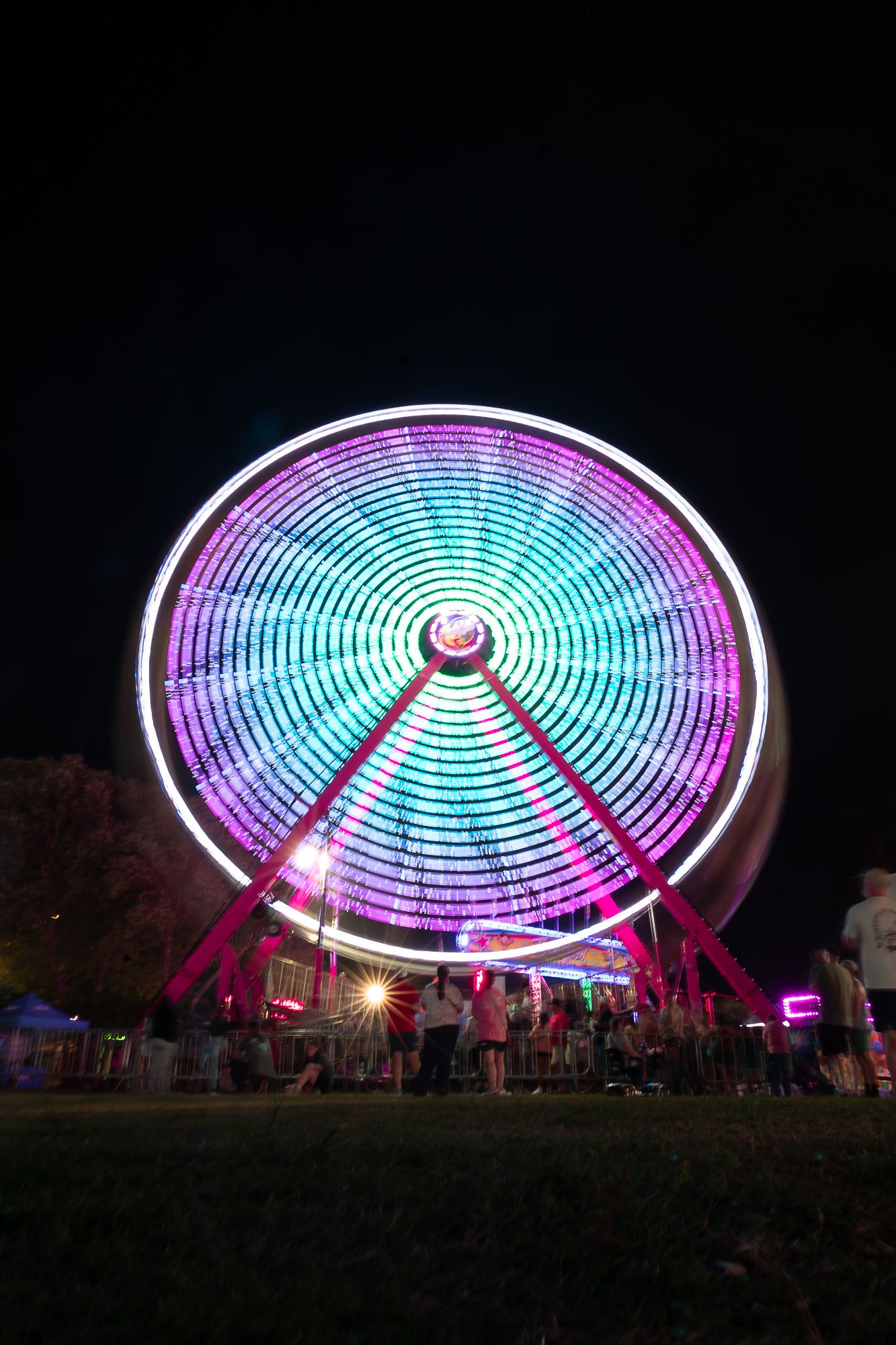 Colorful illuminated Ferris wheel glowing with purple and blue lights against dark night sky.