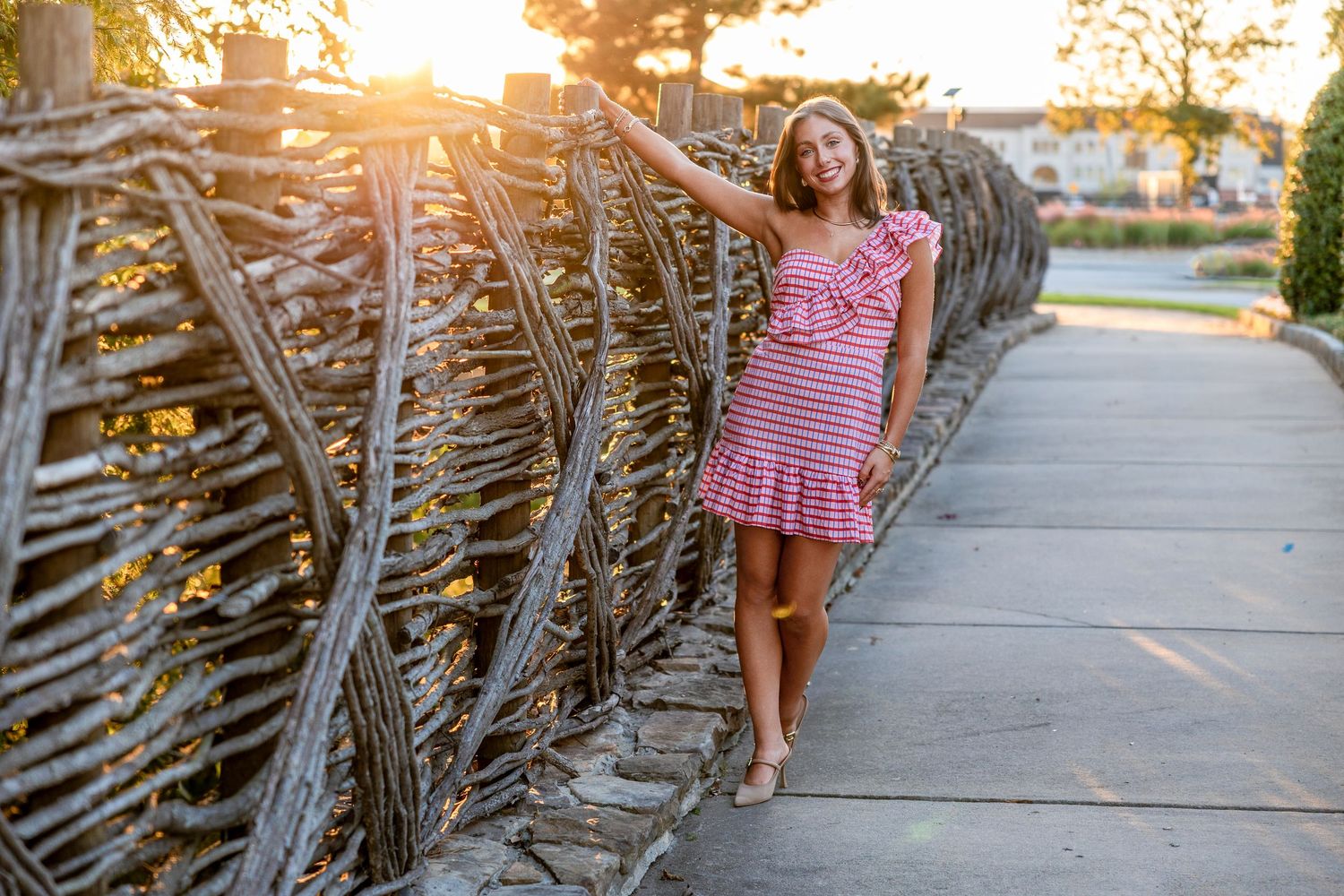 A person in a pink striped dress walks along a sidewalk at sunset with palm fronds creating shadows.