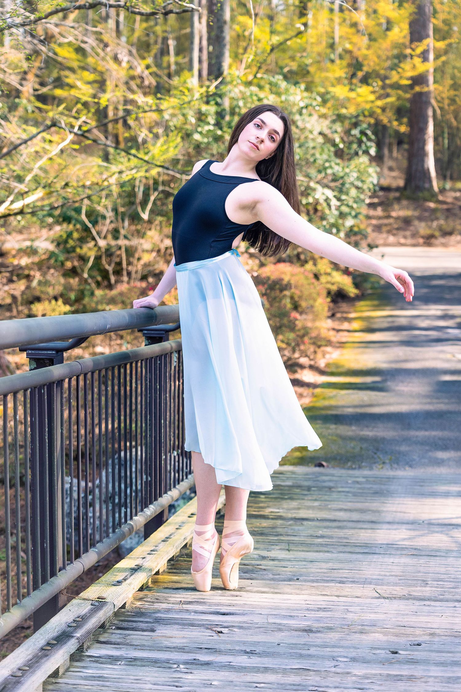 Dancer in white dress performs elegant poses on a wooden bridge surrounded by autumn foliage.