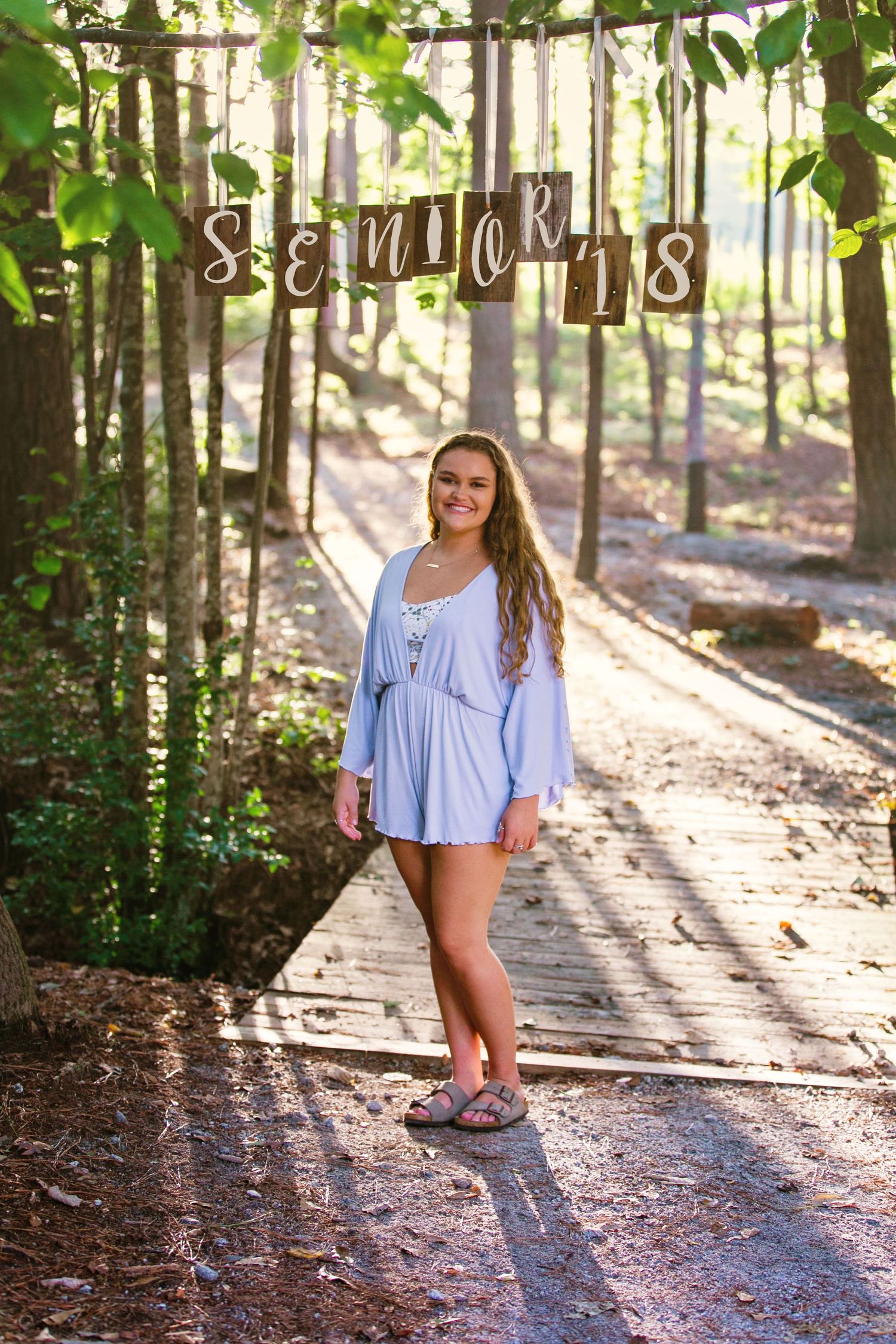 Outdoor portrait session on wooded path with dappled sunlight filtering through trees.