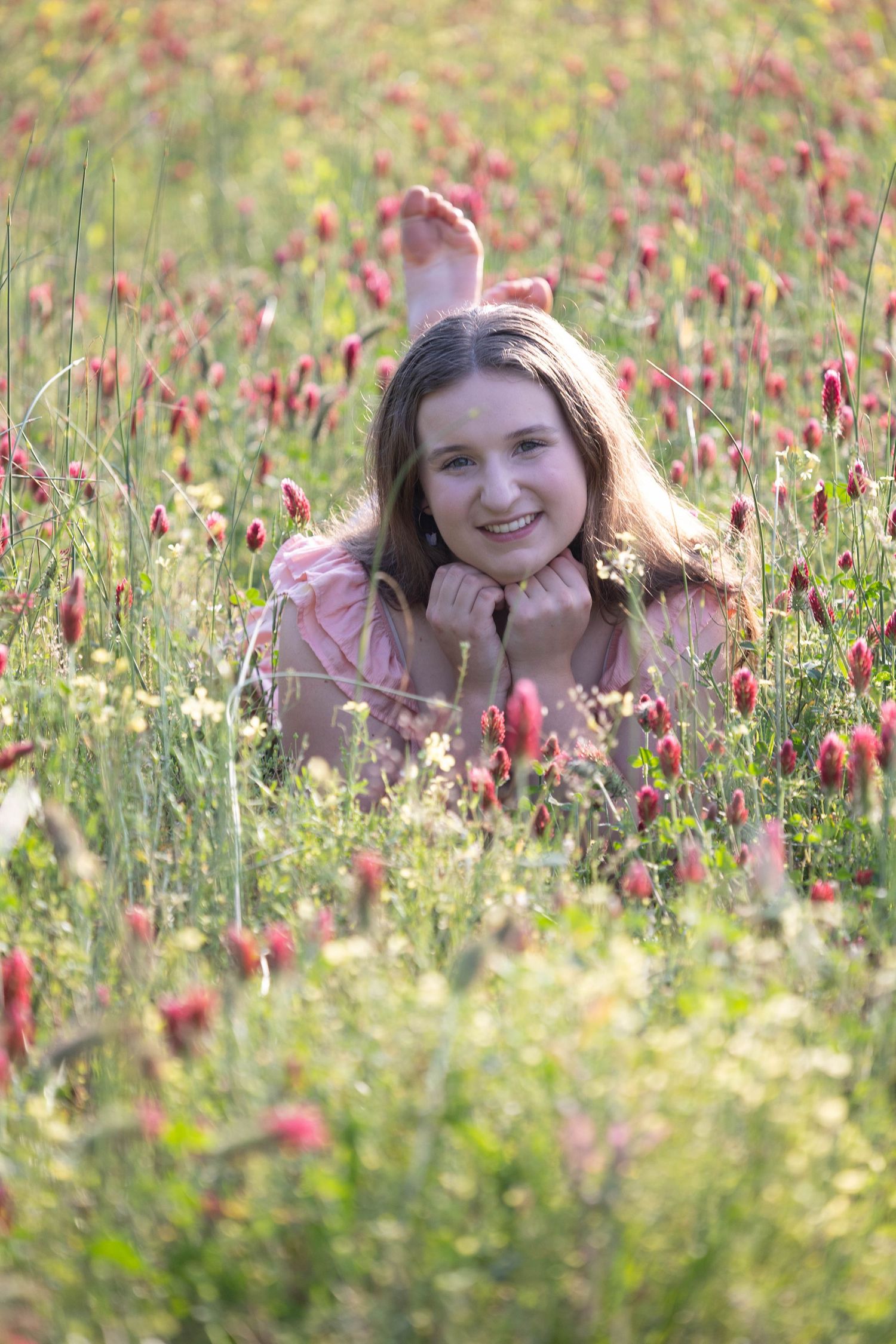 A person lying in a vibrant meadow of red wildflowers during golden hour sunlight.