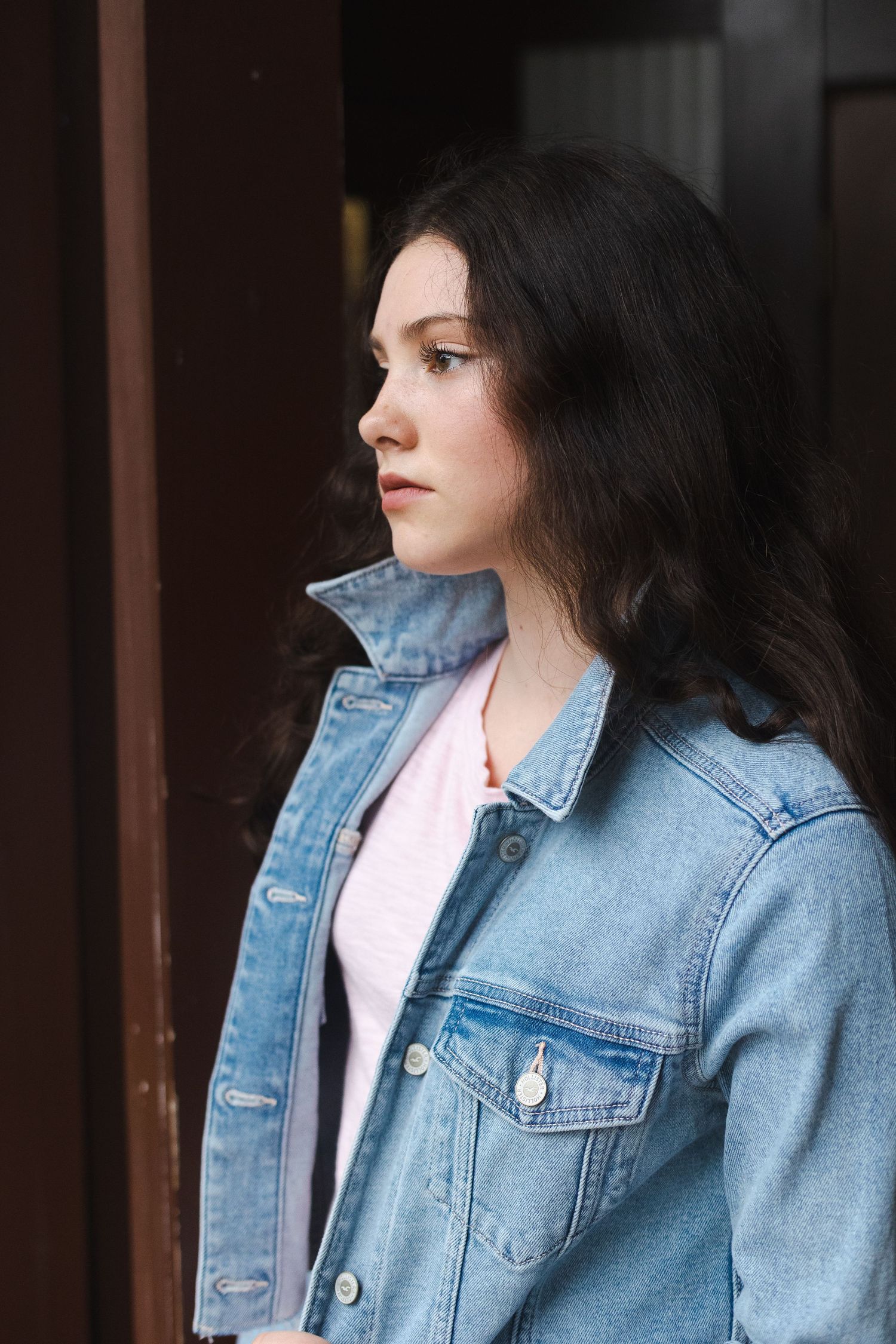 Person wearing light denim jacket poses outdoors near wooden panels.