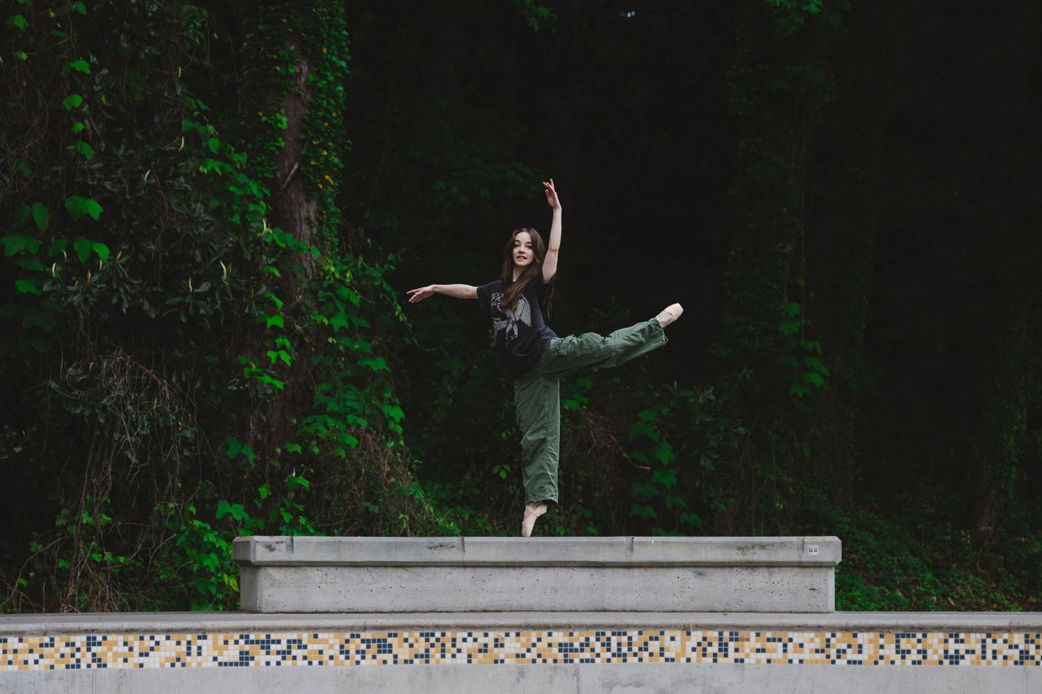 Individual performing acrobatic leap against dark background with green foliage.