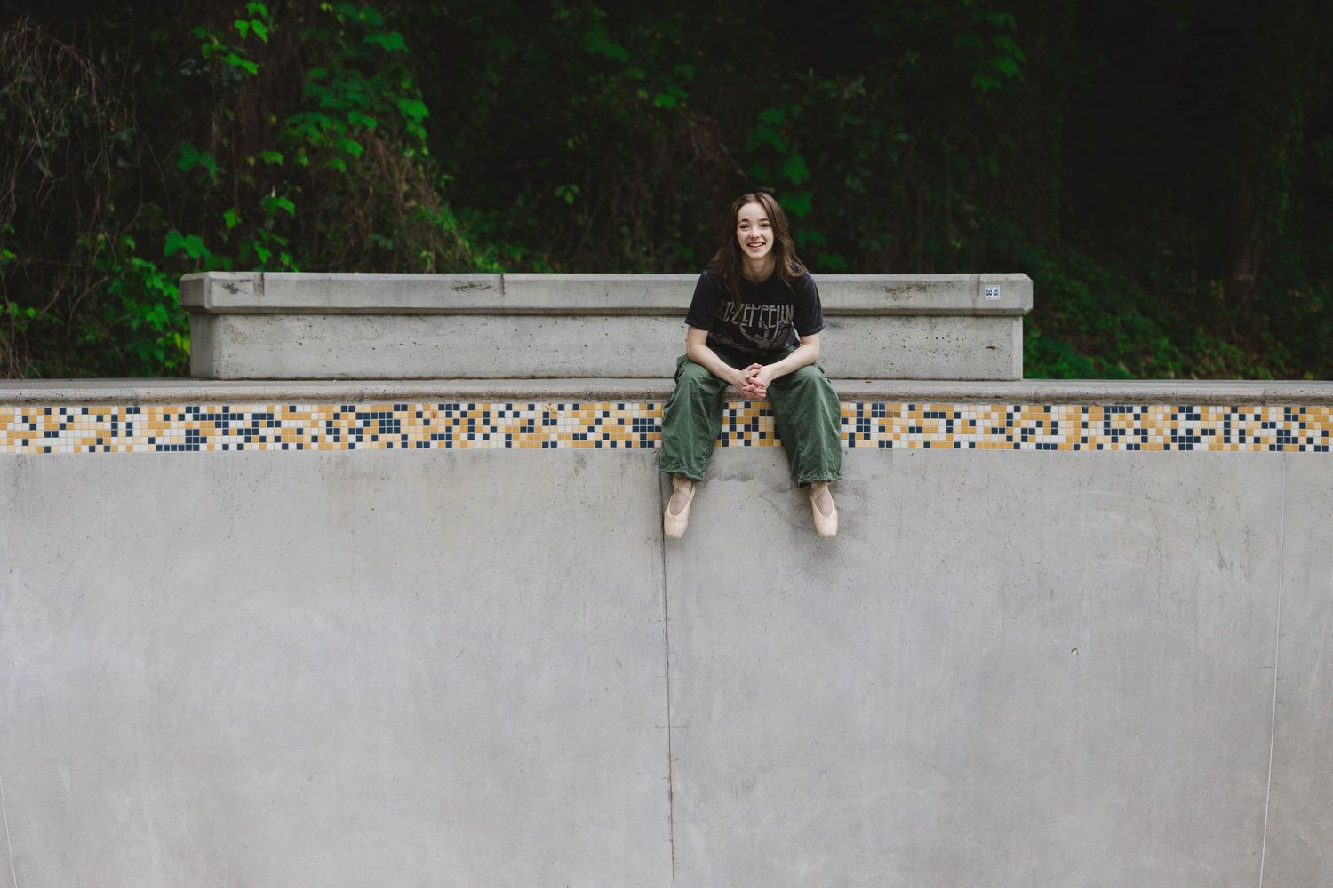 A person sits on a concrete wall surrounded by lush greenery in an outdoor setting.
