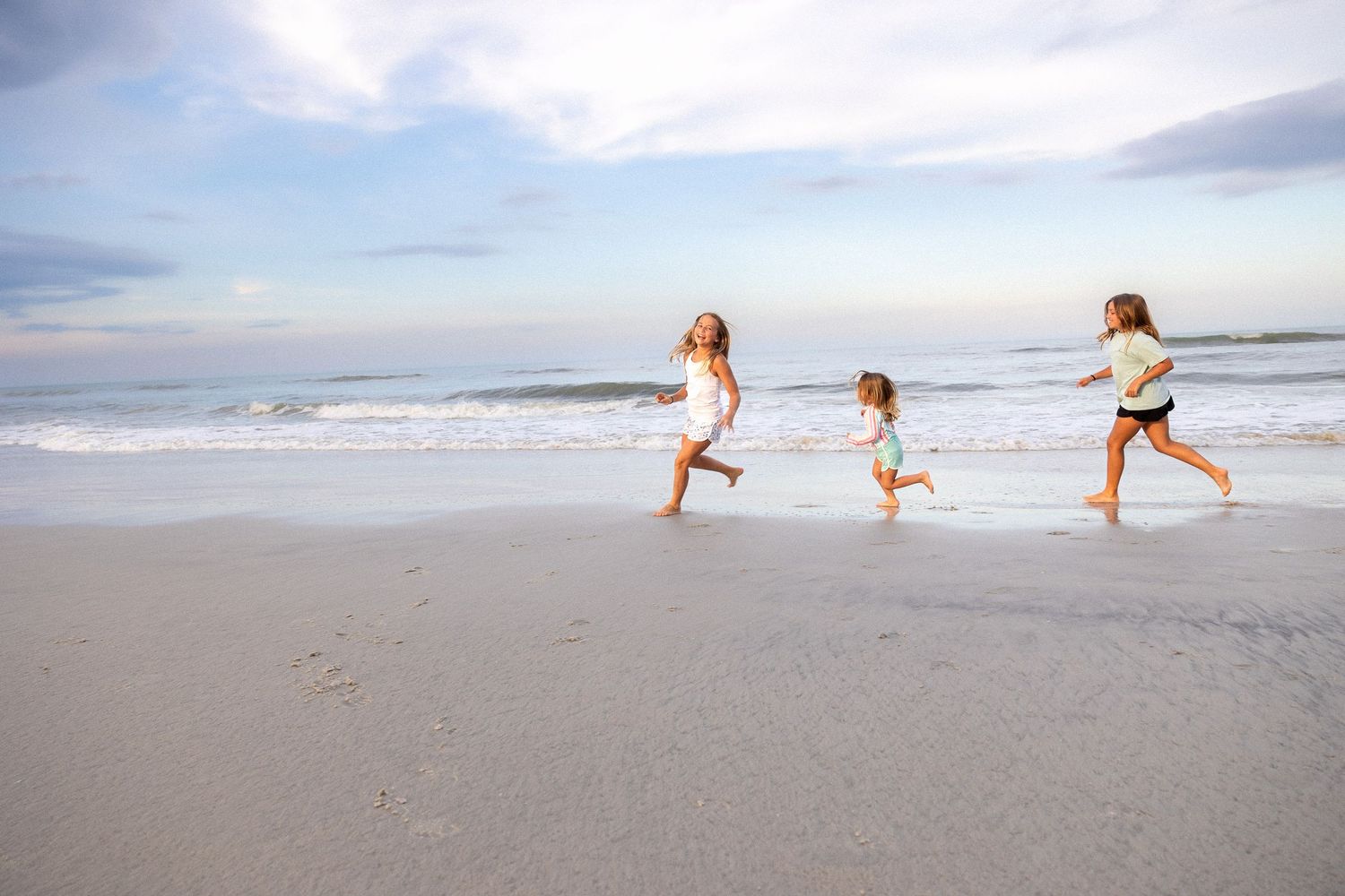 Silhouettes of people running and playing on wide sandy beach at dusk.