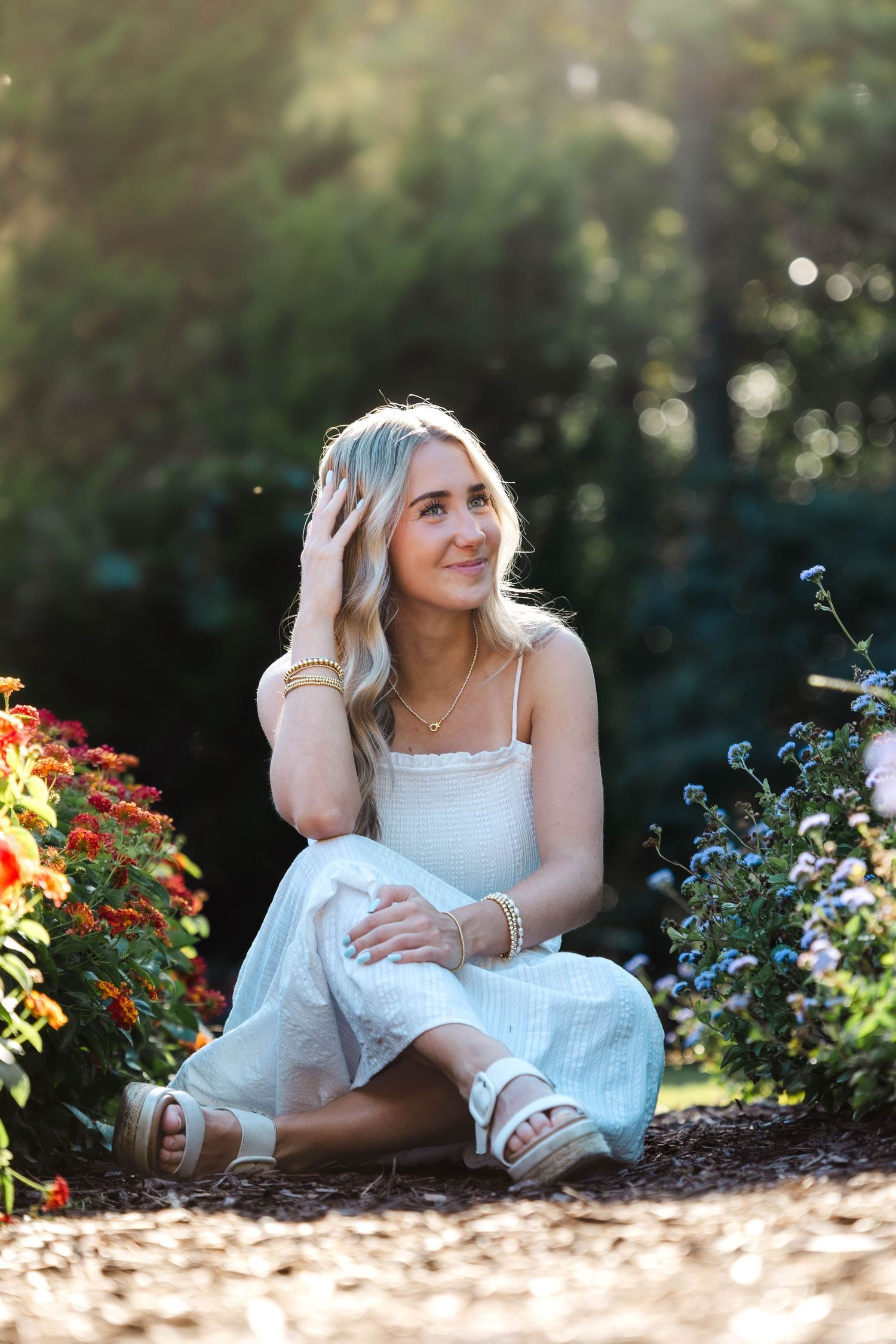 Person in white dress relaxes among colorful garden flowers.
