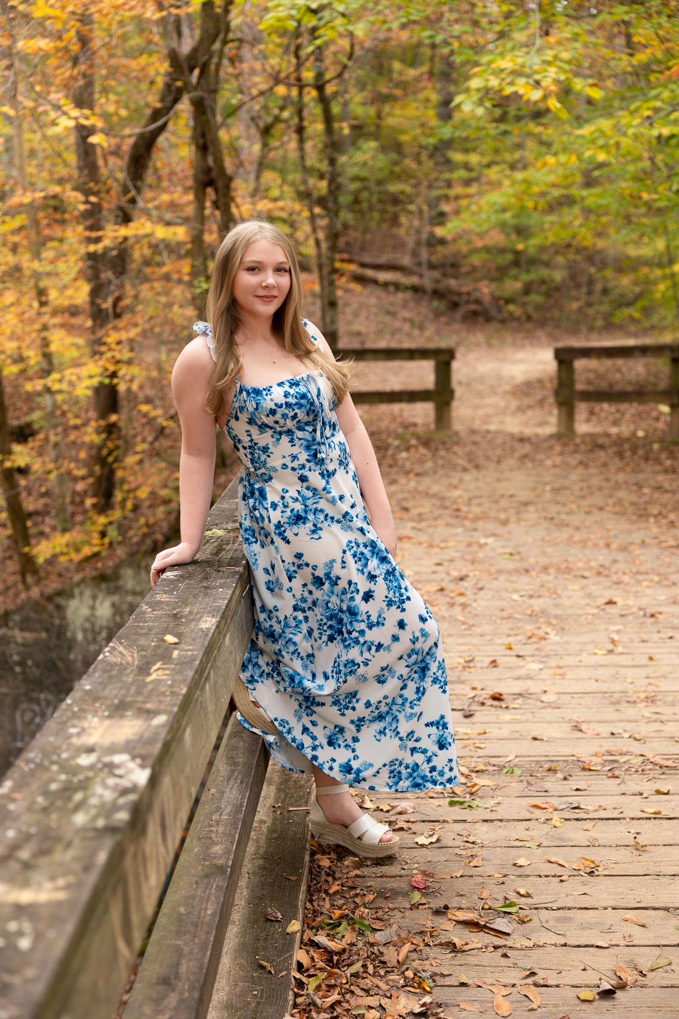 A blue and white floral sundress photographed on a wooden boardwalk surrounded by autumn foliage.