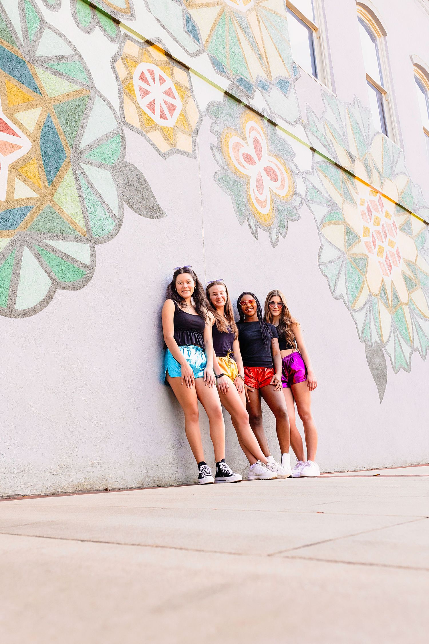 Group of friends sitting against colorful geometric wall mural in casual summer outfits.