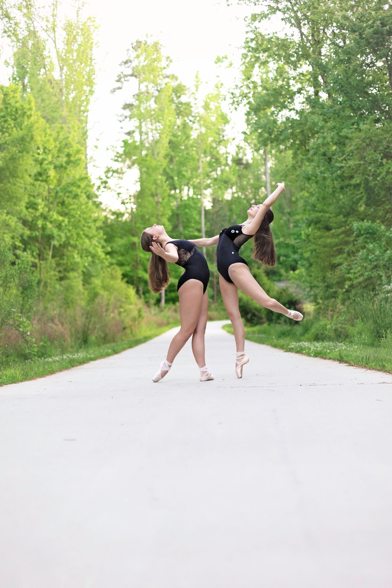 Contemporary dancer performing dynamic movements on outdoor path surrounded by trees.
