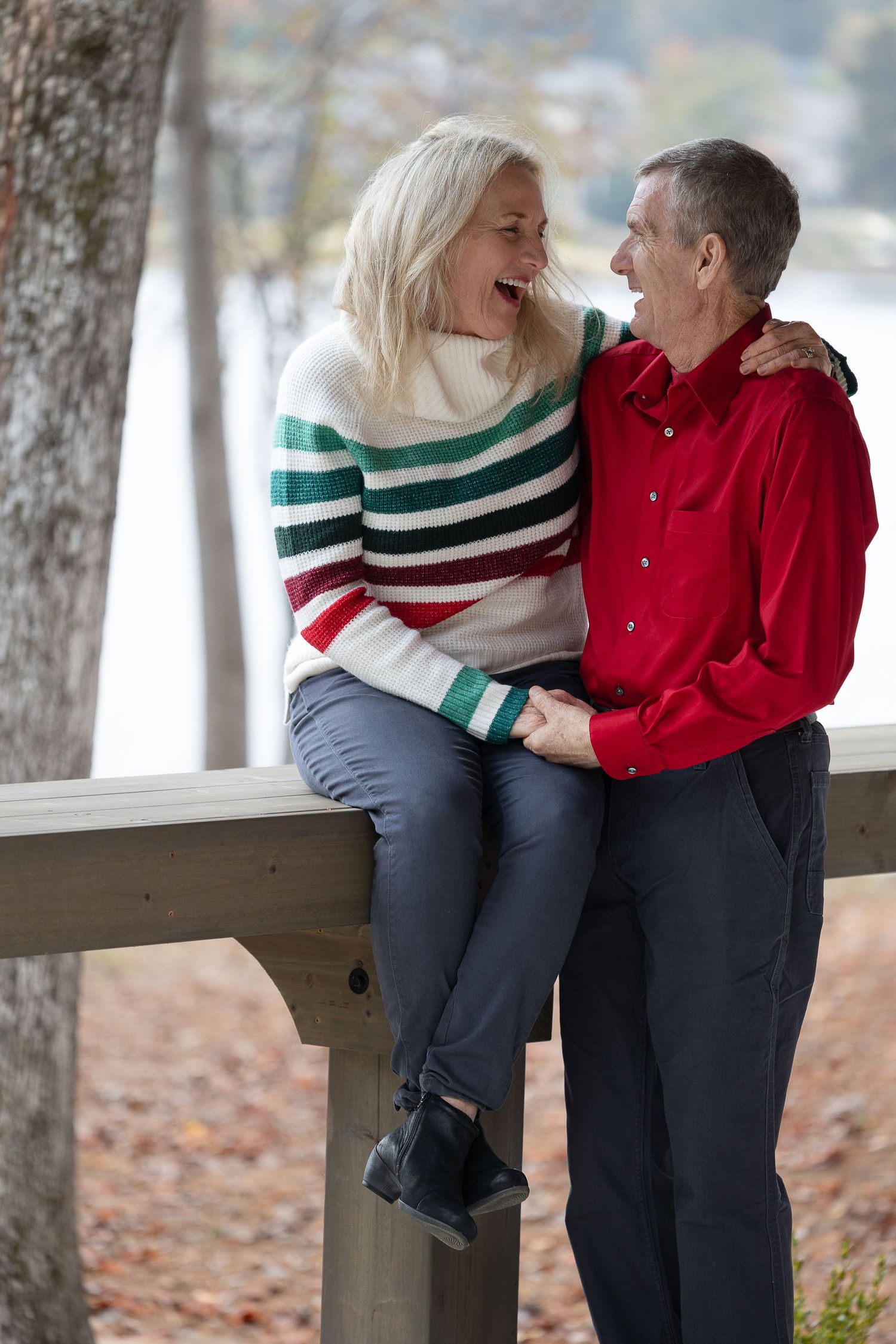 Couple shares joyful moment on wooden bench in winter forest setting.